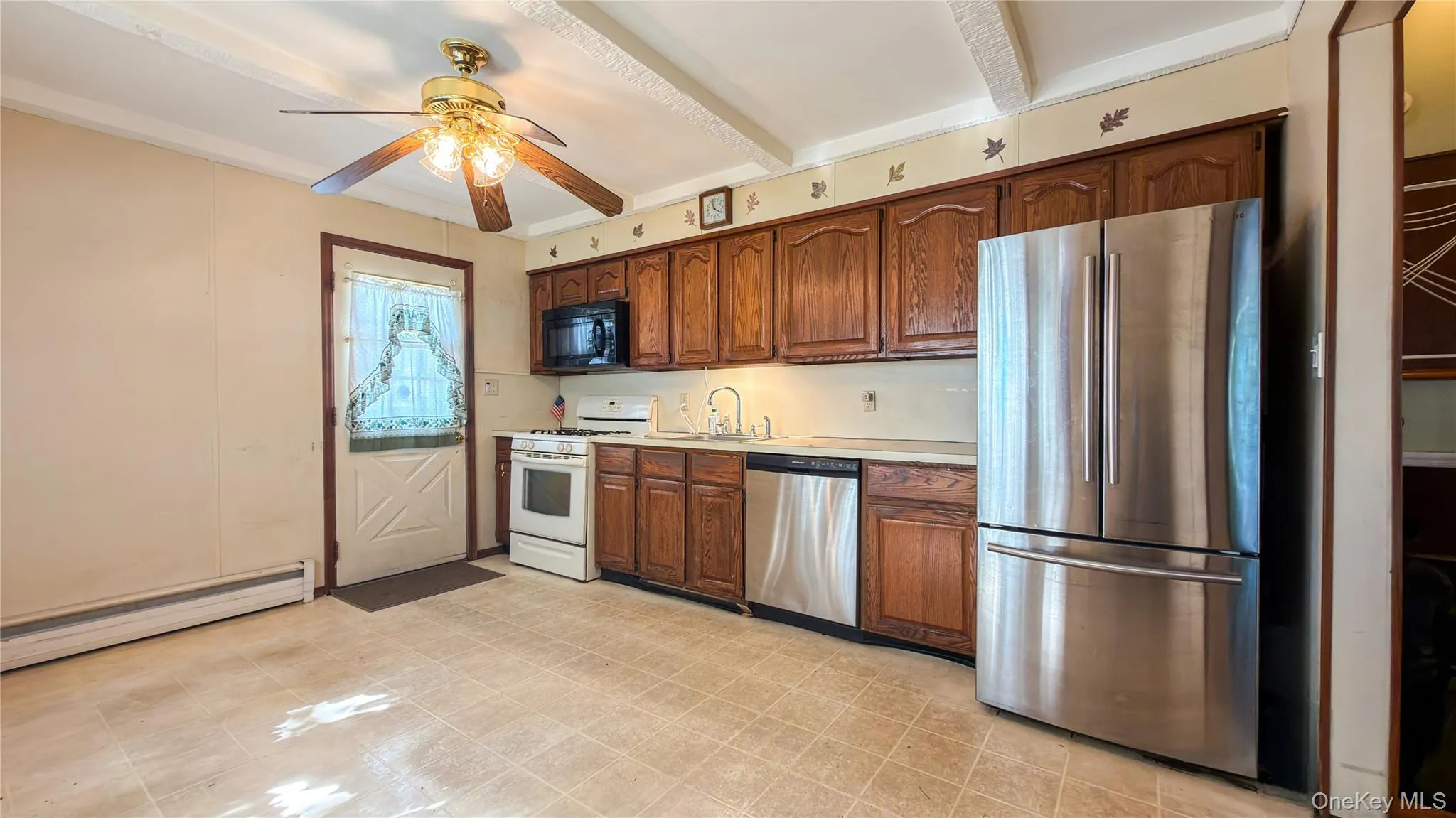 Eat-in-kitchen with wood cabinets, stainless steel refrigerator and dishwasher, white gas stove, black microwave with white painted beam ceiling, ceiling fan, linoleum floors and door leading to the side of the house Eat-in-kitchen with wood cabinets, stainless steel refrigerator and dishwasher, white gas stove, black microwave with white painted beam ceiling, ceiling fan, linoleum floors and door leading to the side of the house