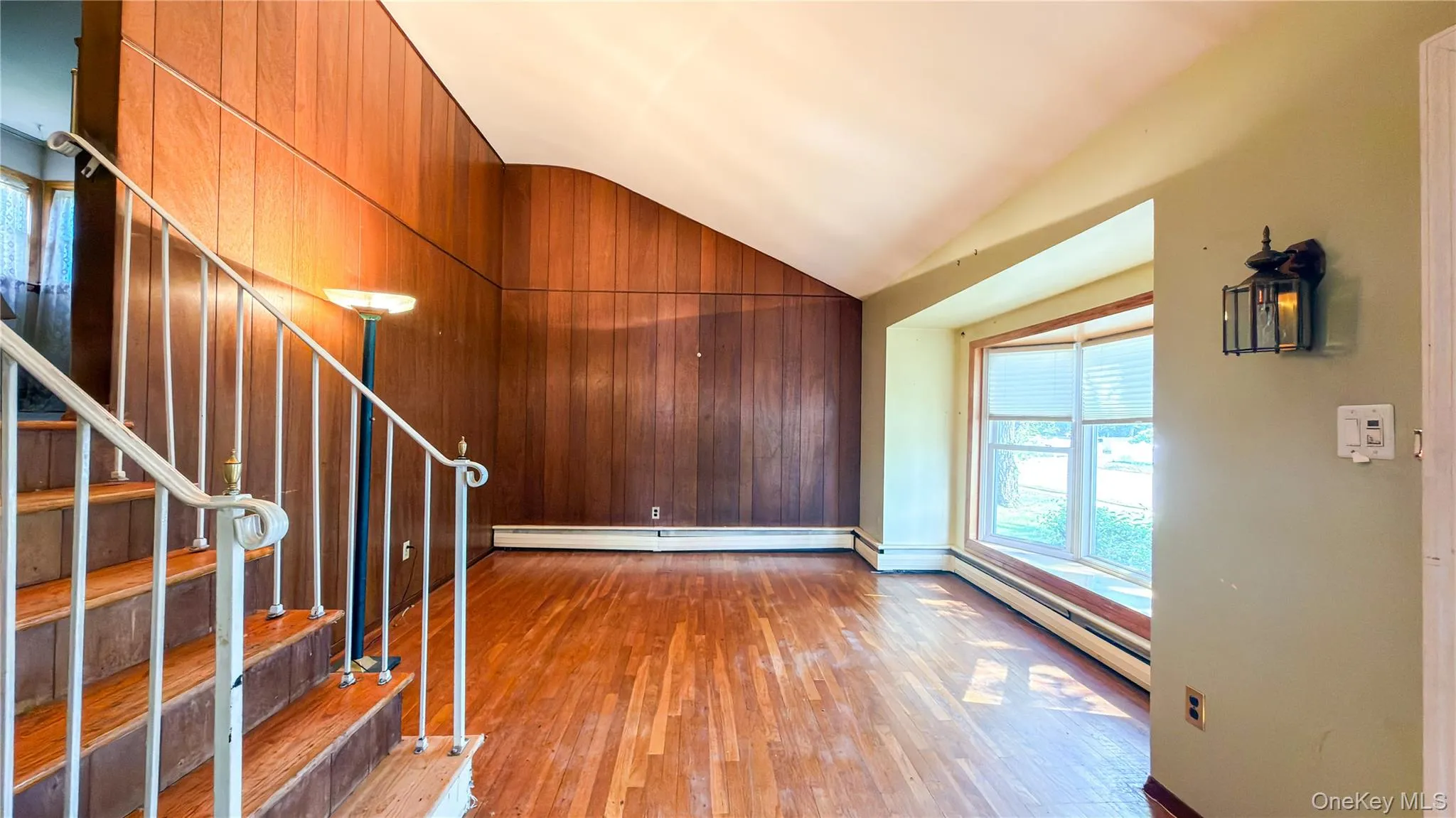 Living room with bay window, wood floors, wood walls and stairs with metal handrails leading to second floor Living room with bay window, wood floors, wood walls and stairs with metal handrails leading to second floor