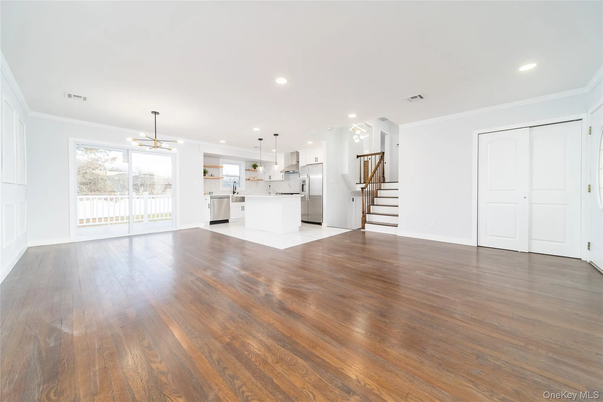 Unfurnished living room with crown molding, stairway, a chandelier, dark wood-style flooring, and recessed lighting Unfurnished living room with crown molding, stairway, a chandelier, dark wood-style flooring, and recessed lighting