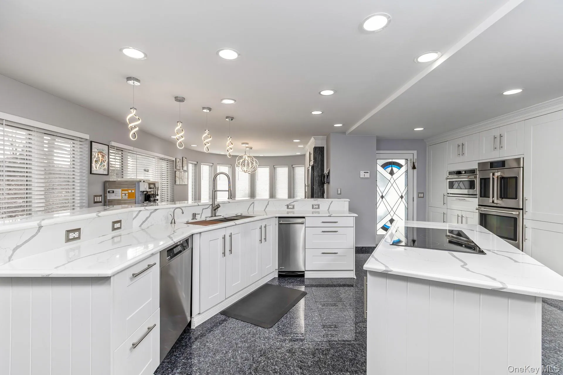 Kitchen featuring a spacious island, white cabinetry, light stone counters, granite tiled floors, and appliances with stainless steel finishes Kitchen featuring a spacious island, white cabinetry, light stone counters, granite tiled floors, and appliances with stainless steel finishes