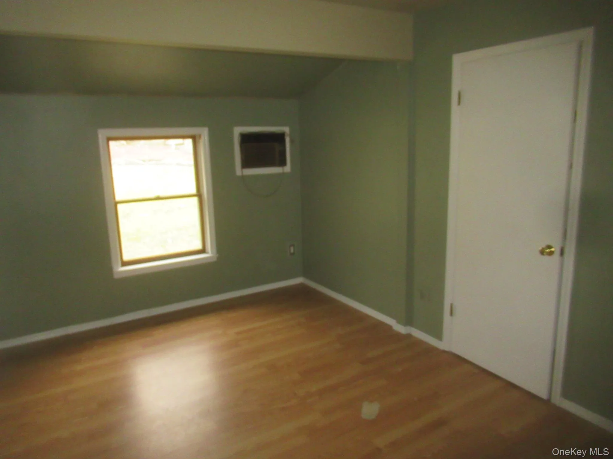 Unfurnished room with wood finished floors, lofted ceiling, and a wall mounted air conditioner Unfurnished room with wood finished floors, lofted ceiling, and a wall mounted air conditioner