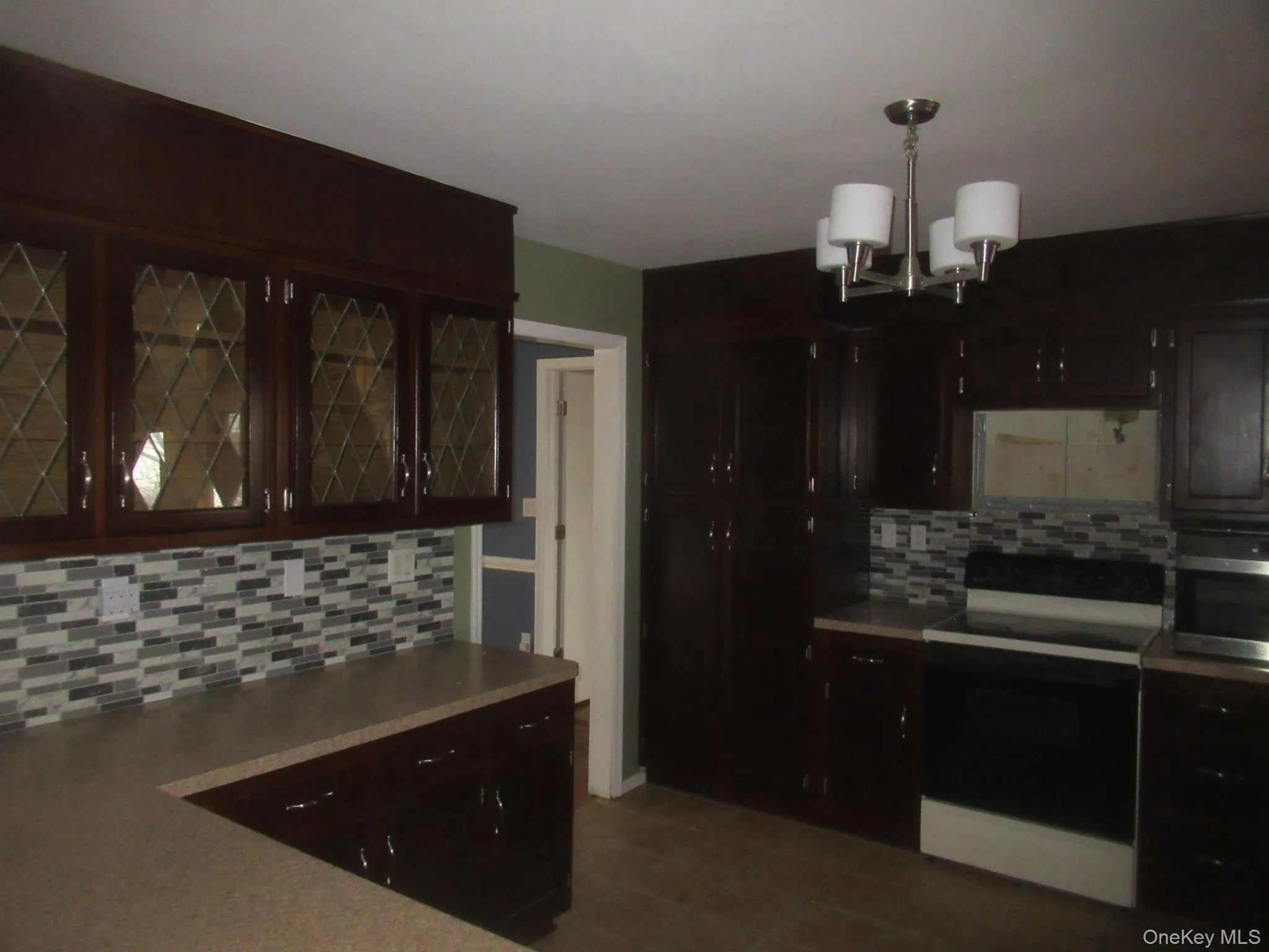Kitchen featuring electric range oven, tasteful backsplash, a chandelier, pendant lighting, and stainless steel microwave Kitchen featuring electric range oven, tasteful backsplash, a chandelier, pendant lighting, and stainless steel microwave