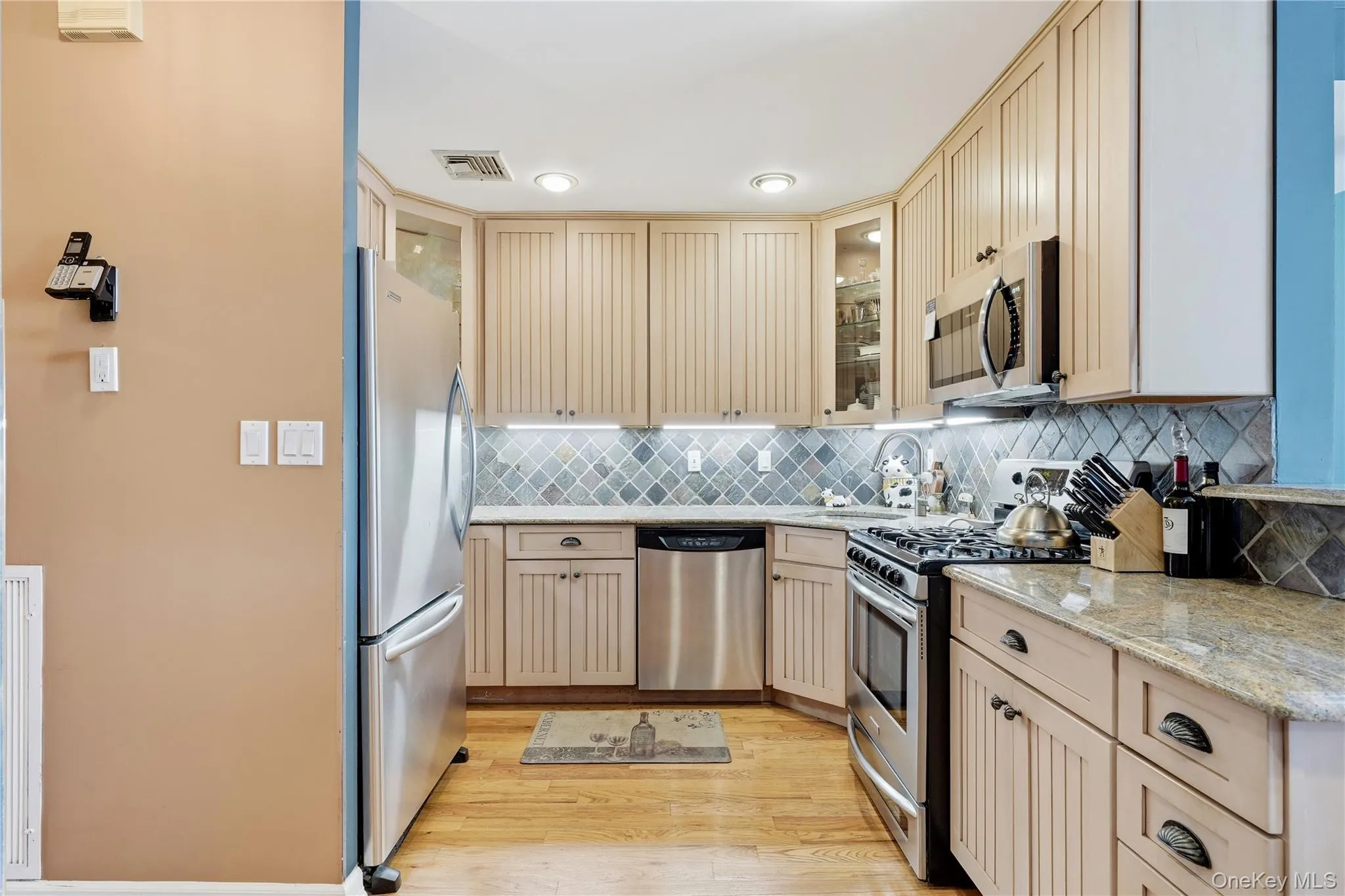 Renovated kitchen featuring stainless steel appliances, custom cabinetry, tile backsplash, and natural stone countertops Renovated kitchen featuring stainless steel appliances, custom cabinetry, tile backsplash, and natural stone countertops