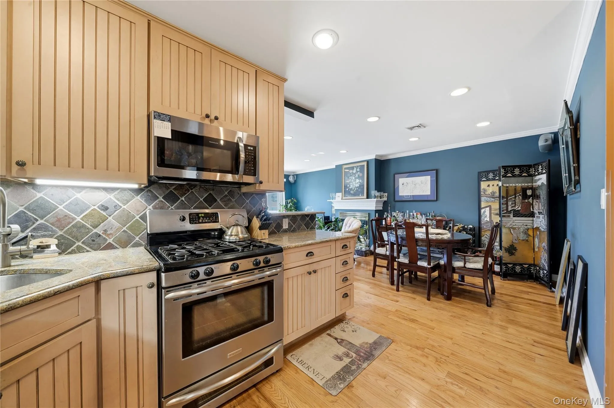 Renovated kitchen featuring stainless steel appliances, custom cabinetry, tile backsplash, and natural stone countertops Renovated kitchen featuring stainless steel appliances, custom cabinetry, tile backsplash, and natural stone countertops