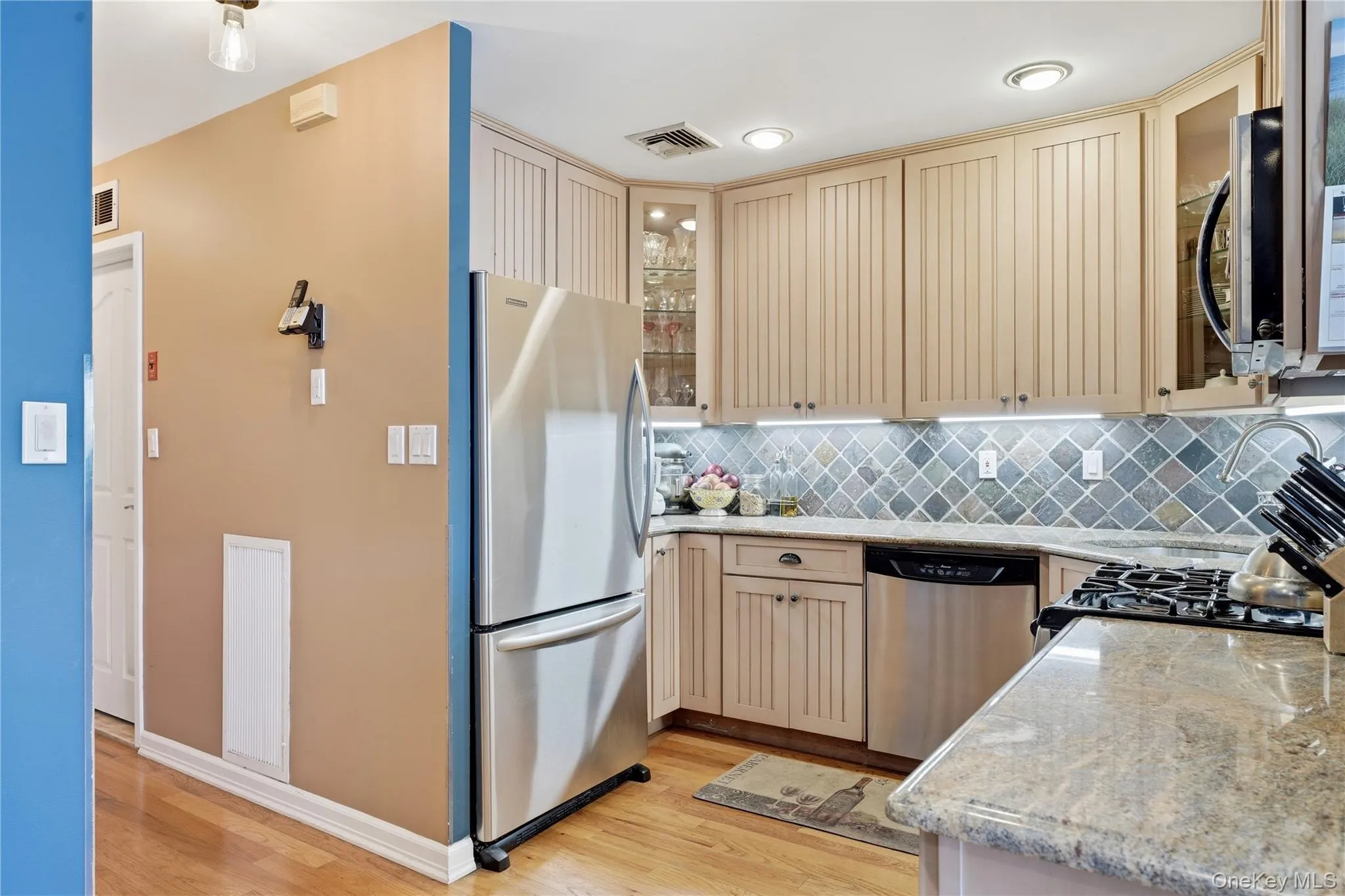 Renovated kitchen featuring stainless steel appliances, custom cabinetry, tile backsplash, and natural stone countertops Renovated kitchen featuring stainless steel appliances, custom cabinetry, tile backsplash, and natural stone countertops