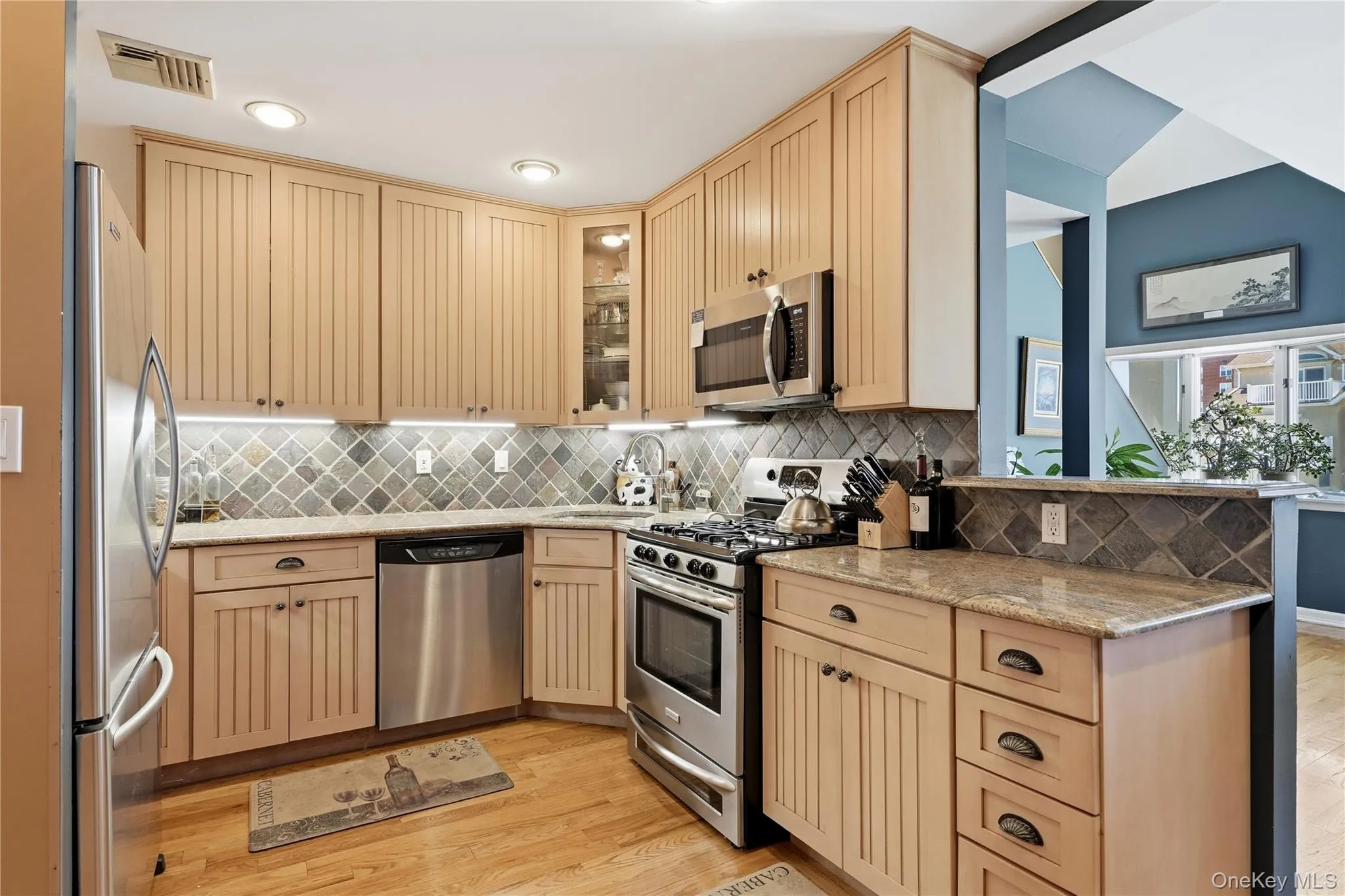 Renovated kitchen featuring stainless steel appliances, custom cabinetry, tile backsplash, and natural stone countertops Renovated kitchen featuring stainless steel appliances, custom cabinetry, tile backsplash, and natural stone countertops