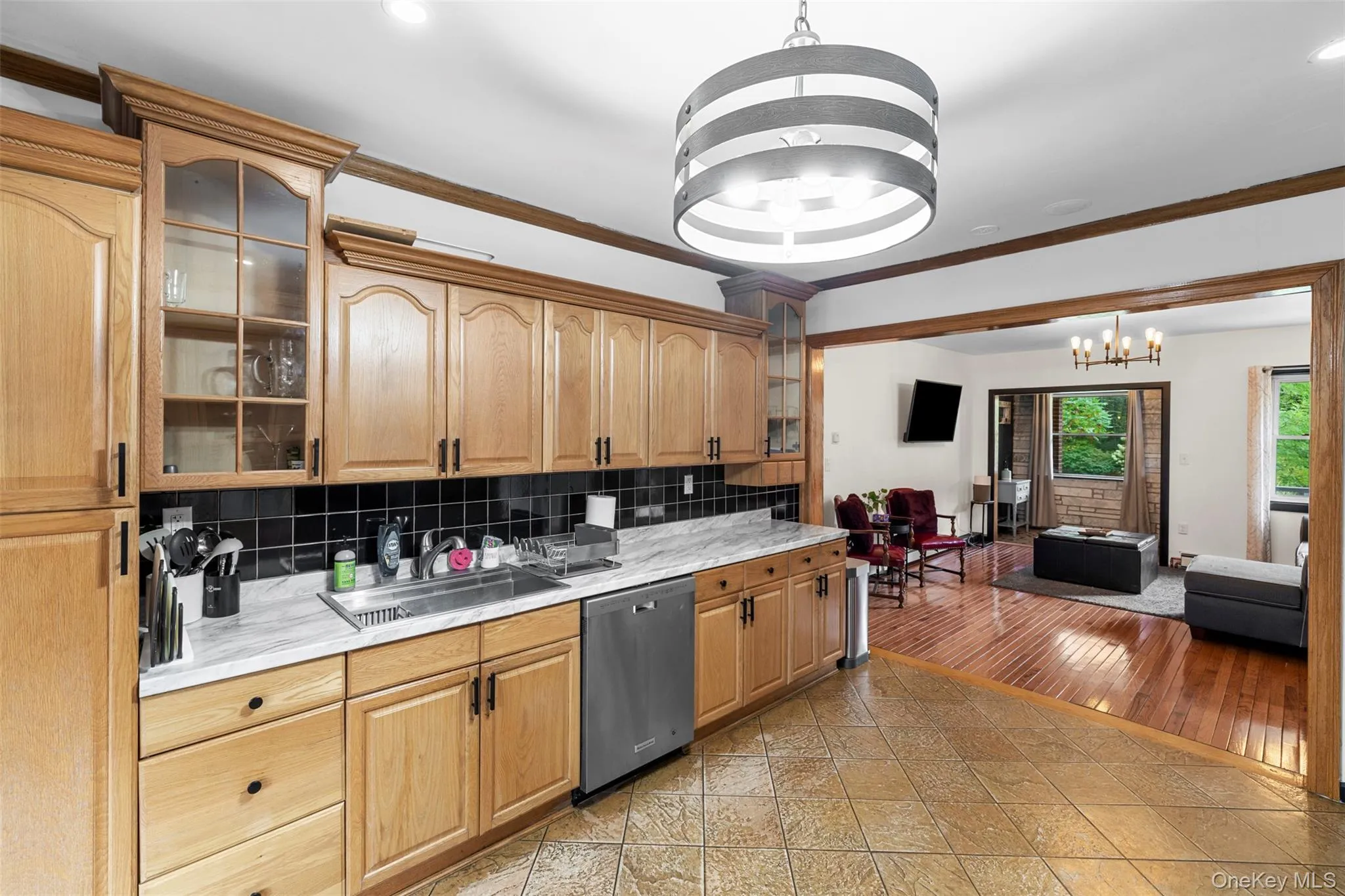Kitchen featuring glass insert cabinets, tasteful backsplash, crown molding, dishwasher, and decorative light fixtures Kitchen featuring glass insert cabinets, tasteful backsplash, crown molding, dishwasher, and decorative light fixtures