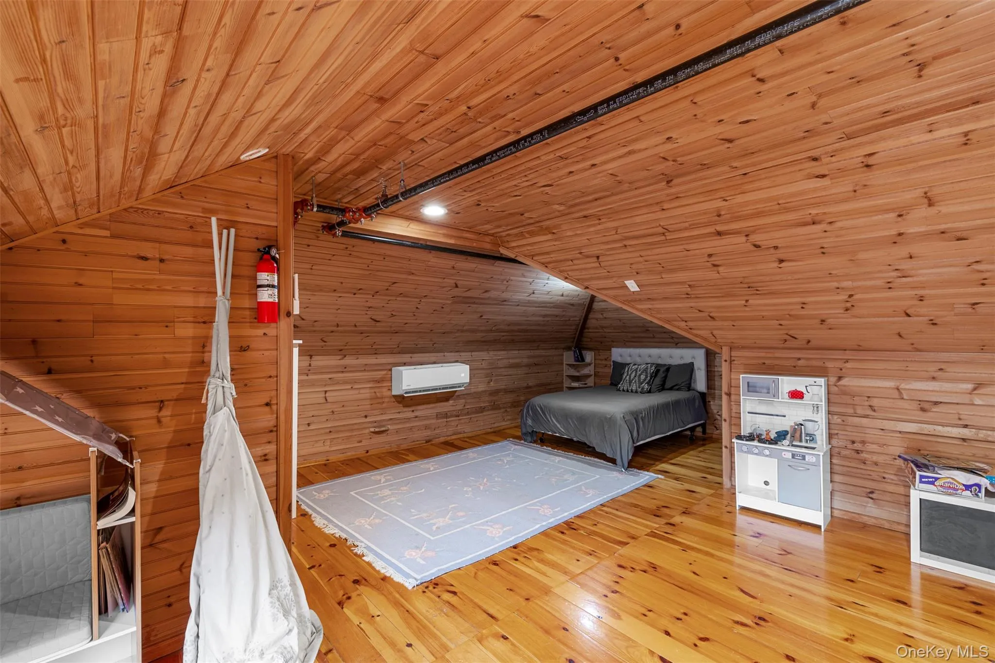 Bedroom with wooden walls, lofted ceiling, wooden ceiling, light wood-style flooring, and a wall mounted air conditioner Bedroom with wooden walls, lofted ceiling, wooden ceiling, light wood-style flooring, and a wall mounted air conditioner