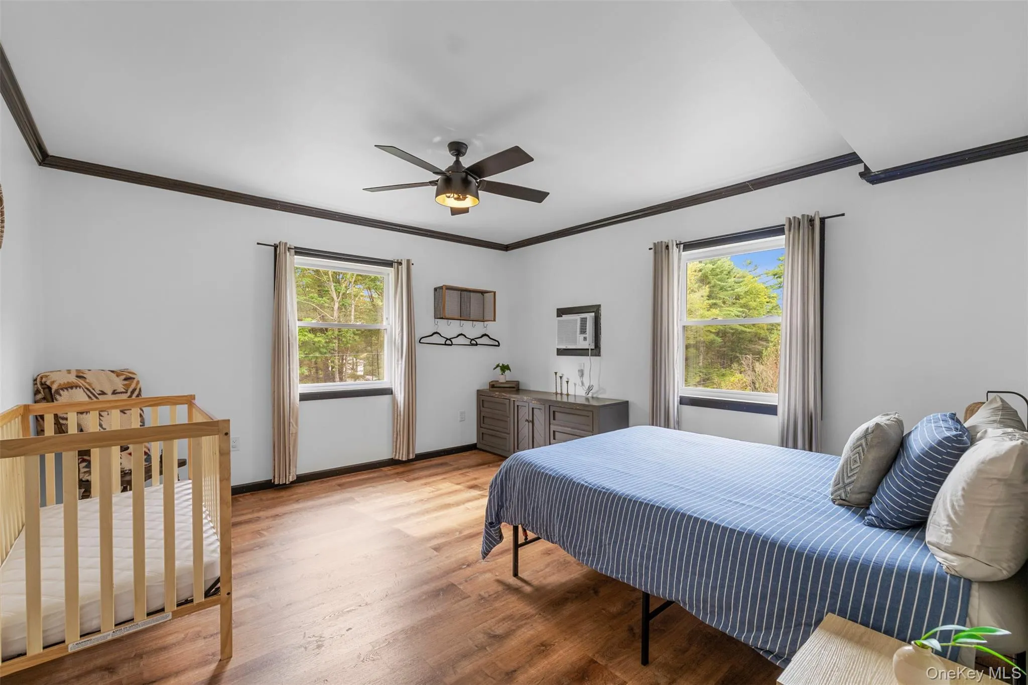 Bedroom with crown molding, wood finished floors, multiple windows, a crib, and a ceiling fan Bedroom with crown molding, wood finished floors, multiple windows, a crib, and a ceiling fan