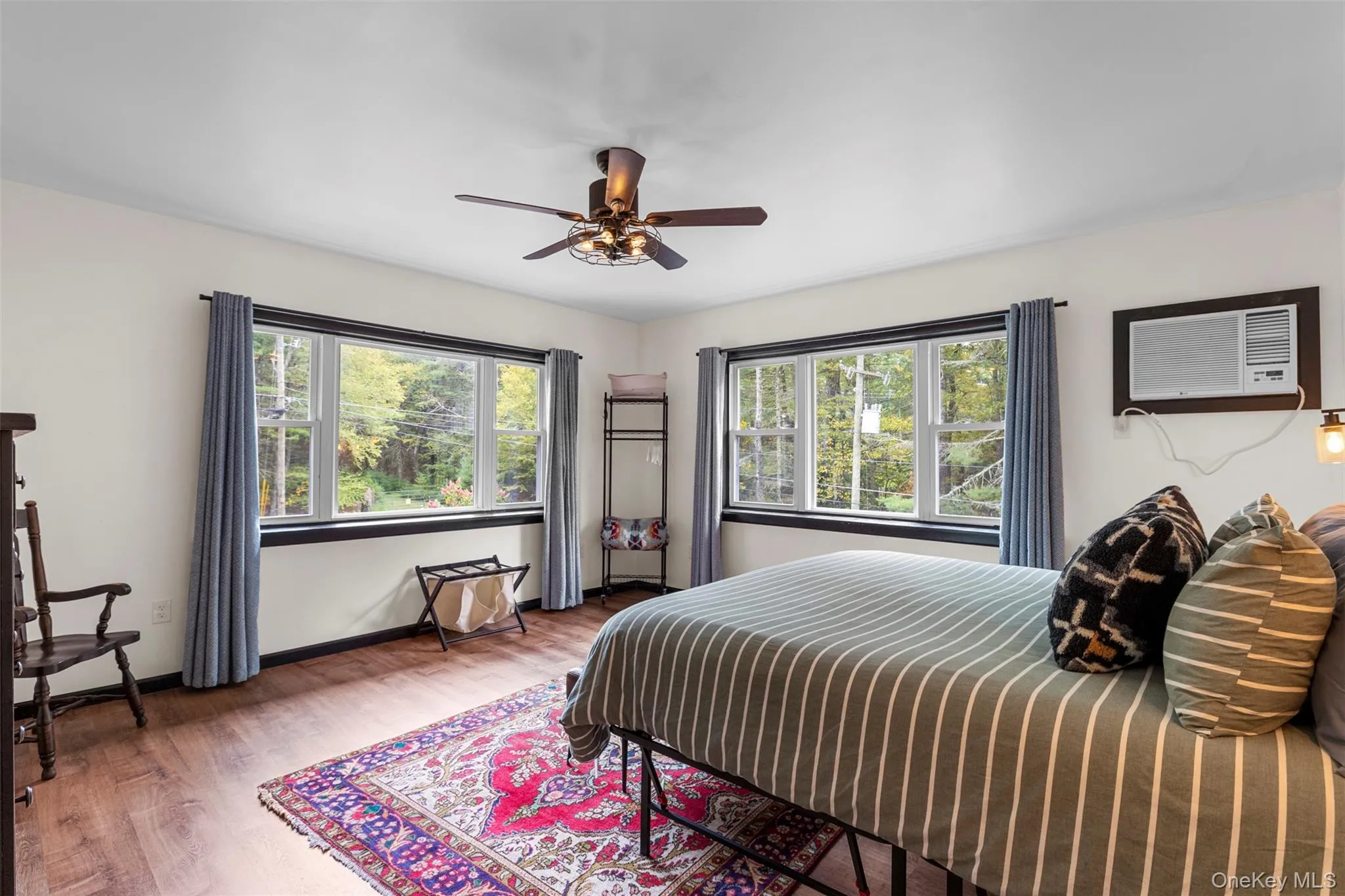 Bedroom featuring multiple windows, wood finished floors, ceiling fan, and a wall unit AC Bedroom featuring multiple windows, wood finished floors, ceiling fan, and a wall unit AC