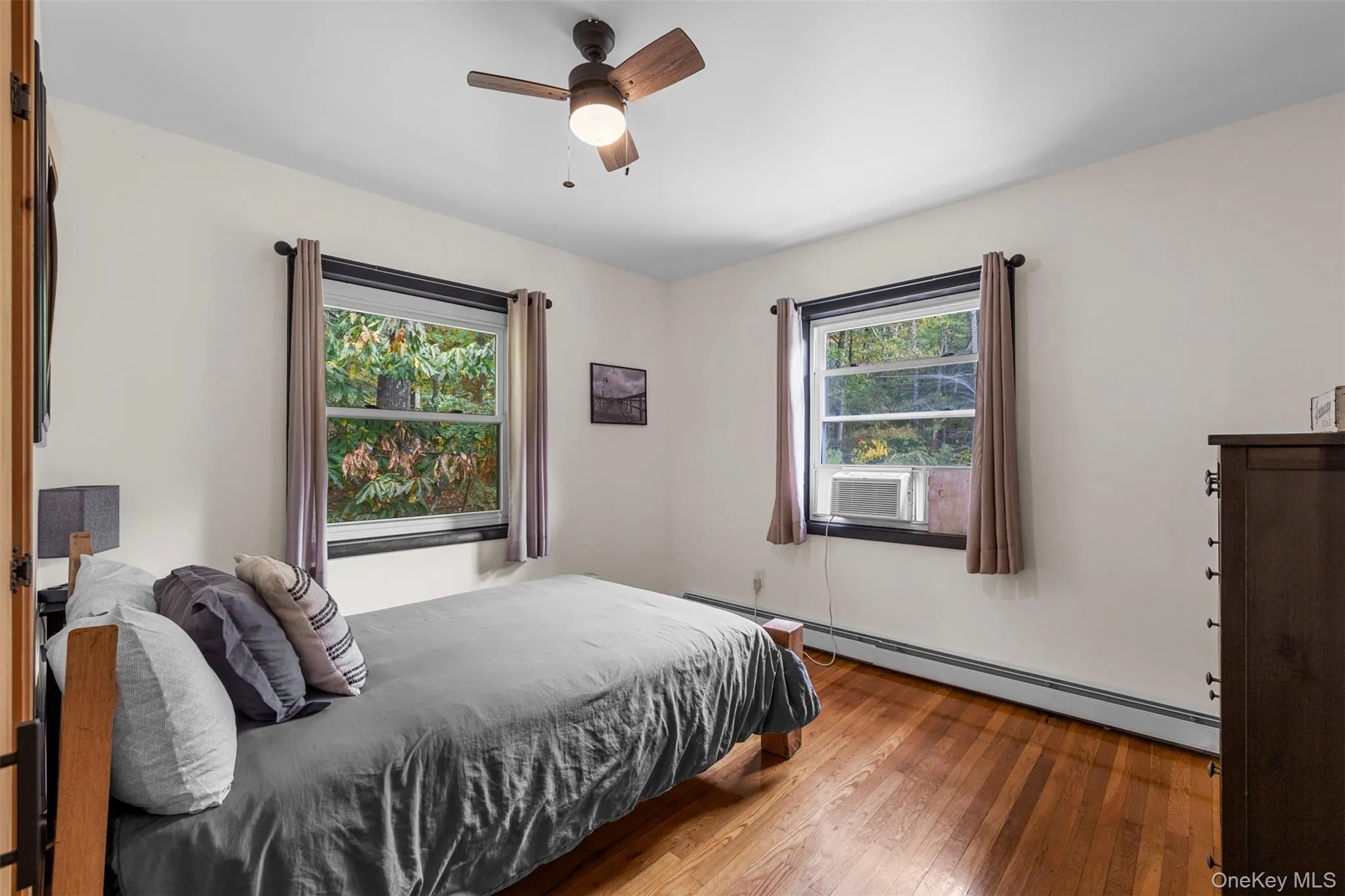 Bedroom with wood-type flooring, baseboard heating, and a ceiling fan Bedroom with wood-type flooring, baseboard heating, and a ceiling fan