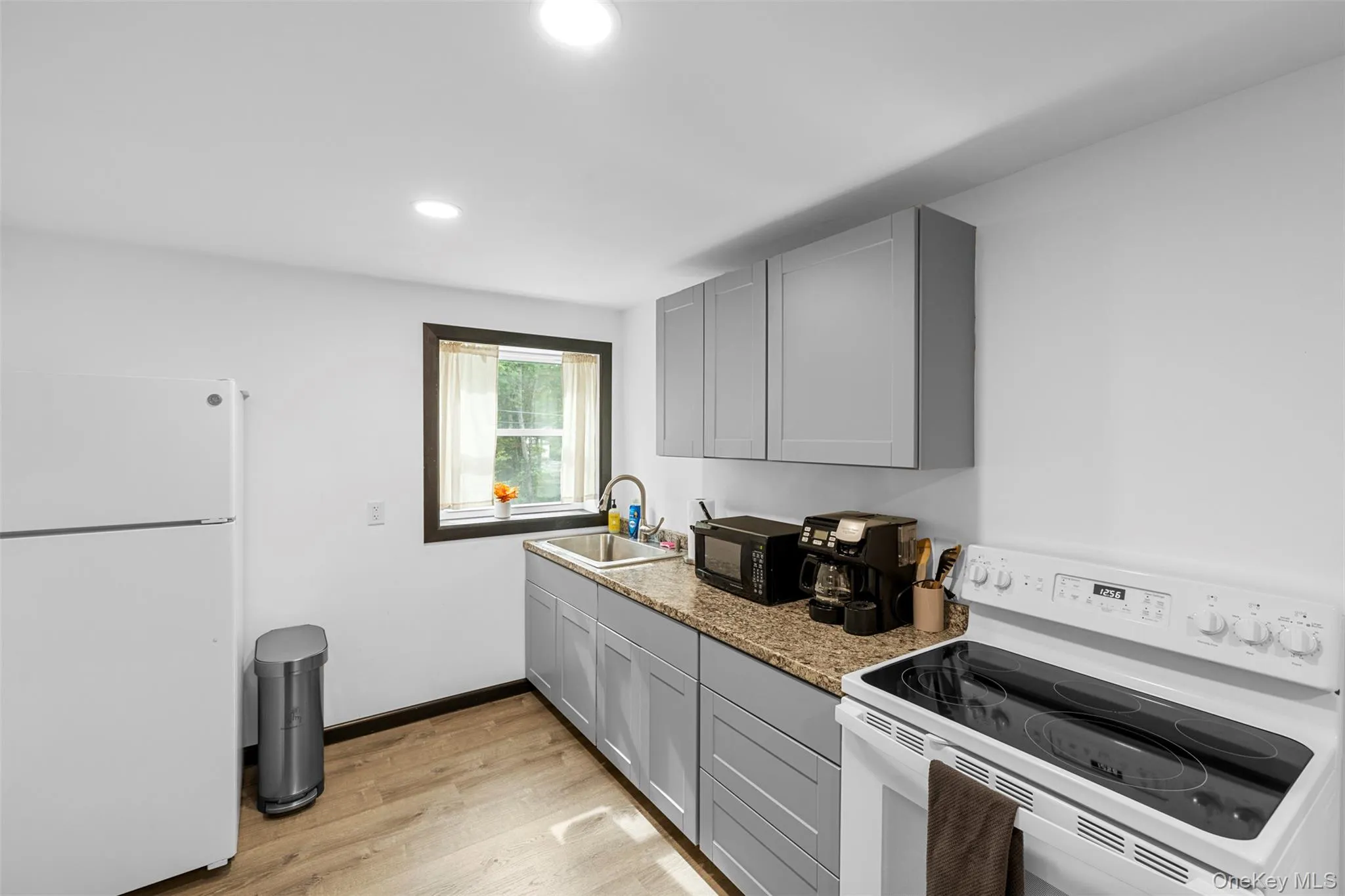 Kitchen featuring white appliances, gray cabinetry, light wood finished floors, light stone countertops, and recessed lighting Kitchen featuring white appliances, gray cabinetry, light wood finished floors, light stone countertops, and recessed lighting