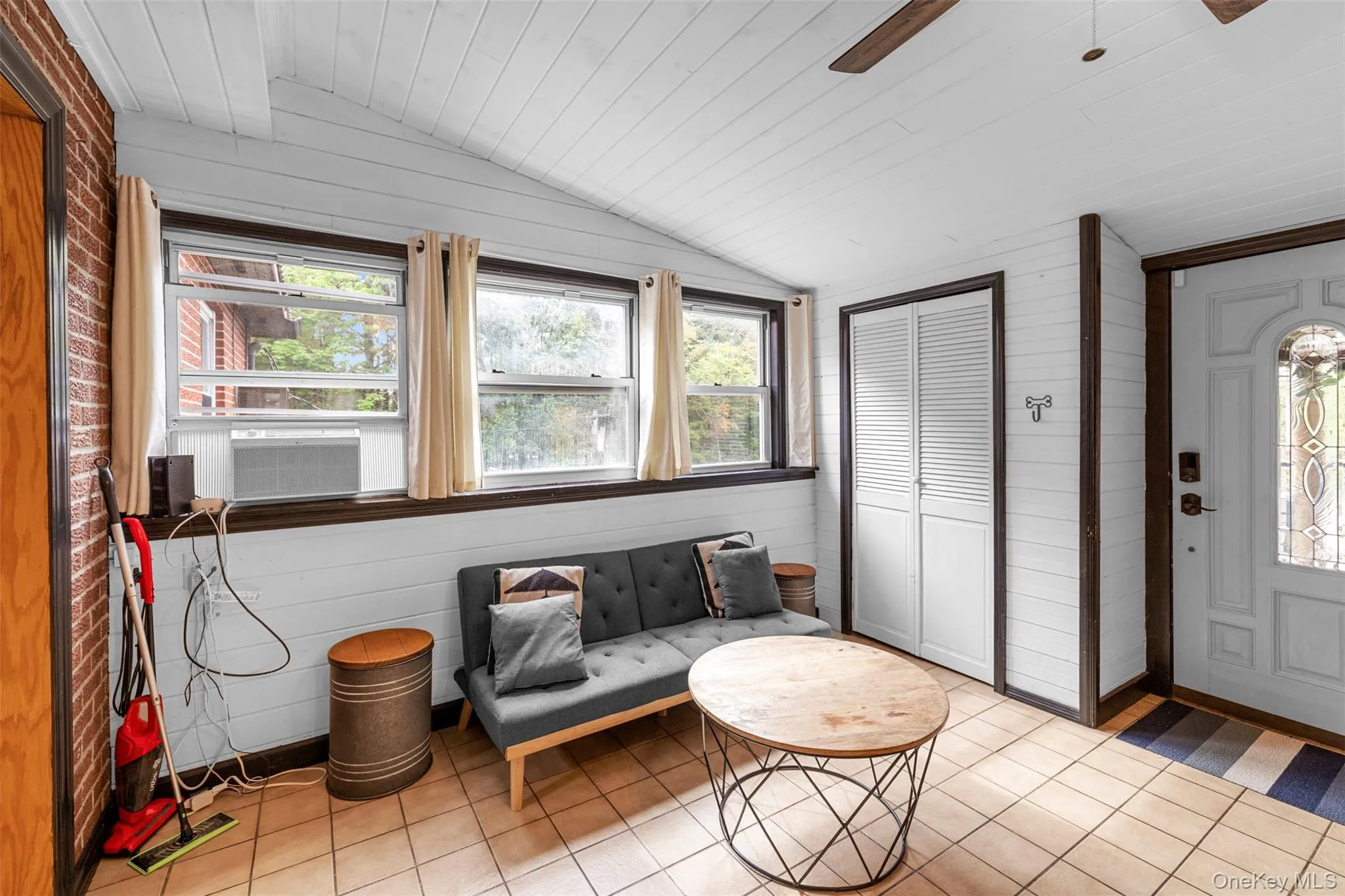 Living area with lofted ceiling, wood walls, light tile patterned floors, healthy amount of natural light, and wood ceiling Living area with lofted ceiling, wood walls, light tile patterned floors, healthy amount of natural light, and wood ceiling