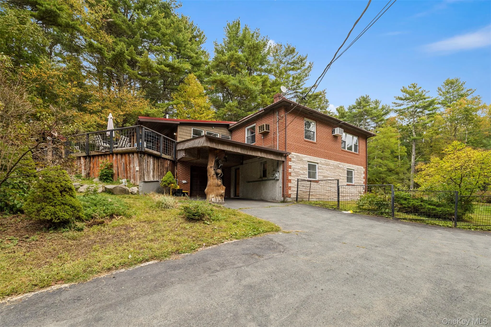 View of front of home featuring driveway, a wooden deck, a chimney, a wall unit AC, and stone siding View of front of home featuring driveway, a wooden deck, a chimney, a wall unit AC, and stone siding