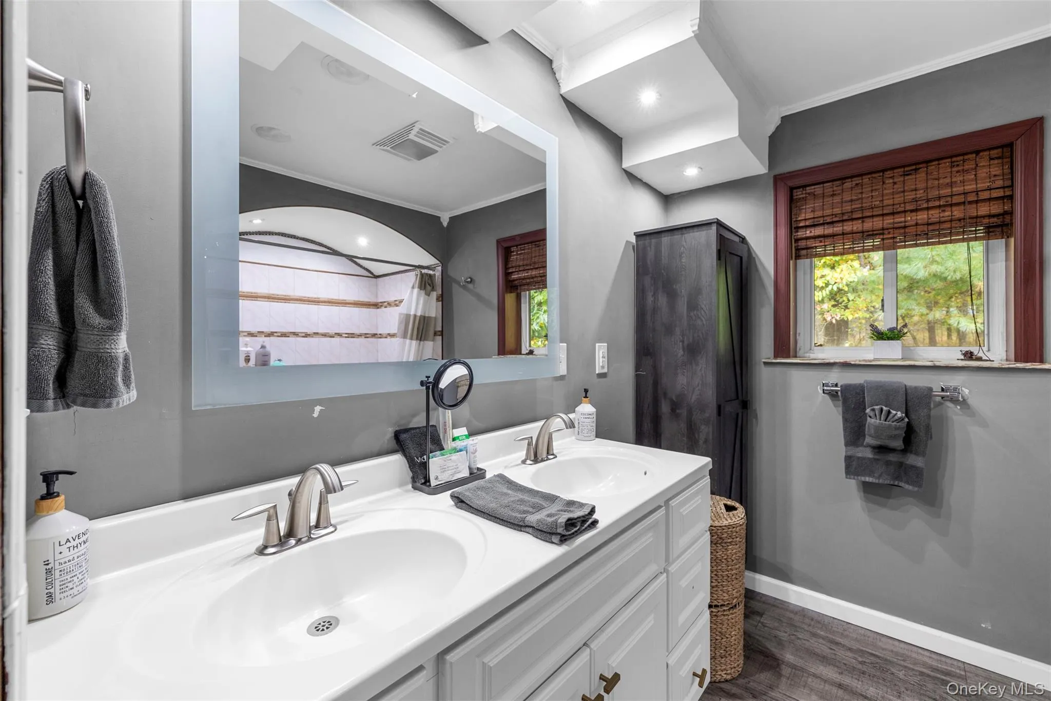 Full bath featuring dark wood-style floors, double vanity, ornamental molding, and curtained shower Full bath featuring dark wood-style floors, double vanity, ornamental molding, and curtained shower