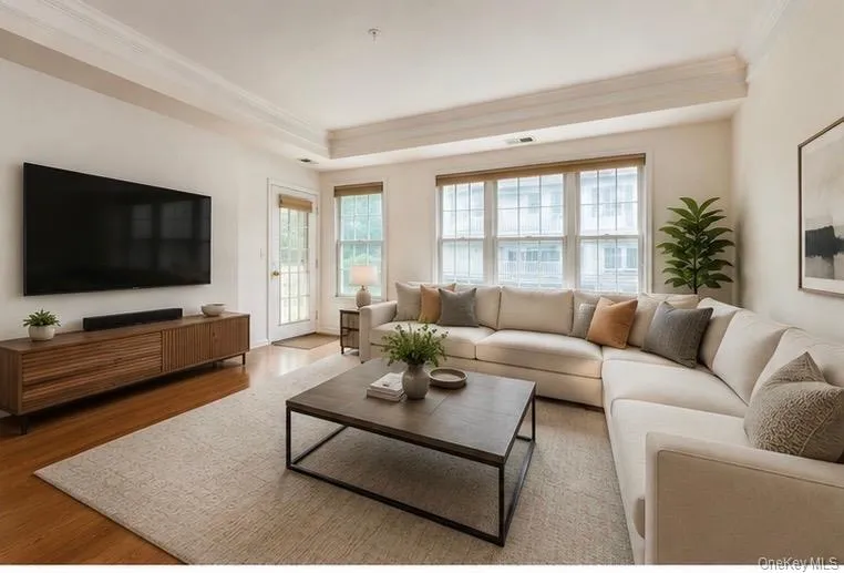 Spacious living area featuring wood-finish flooring, recessed lighting, and a tray ceiling with crown molding Spacious living area featuring wood-finish flooring, recessed lighting, and a tray ceiling with crown molding