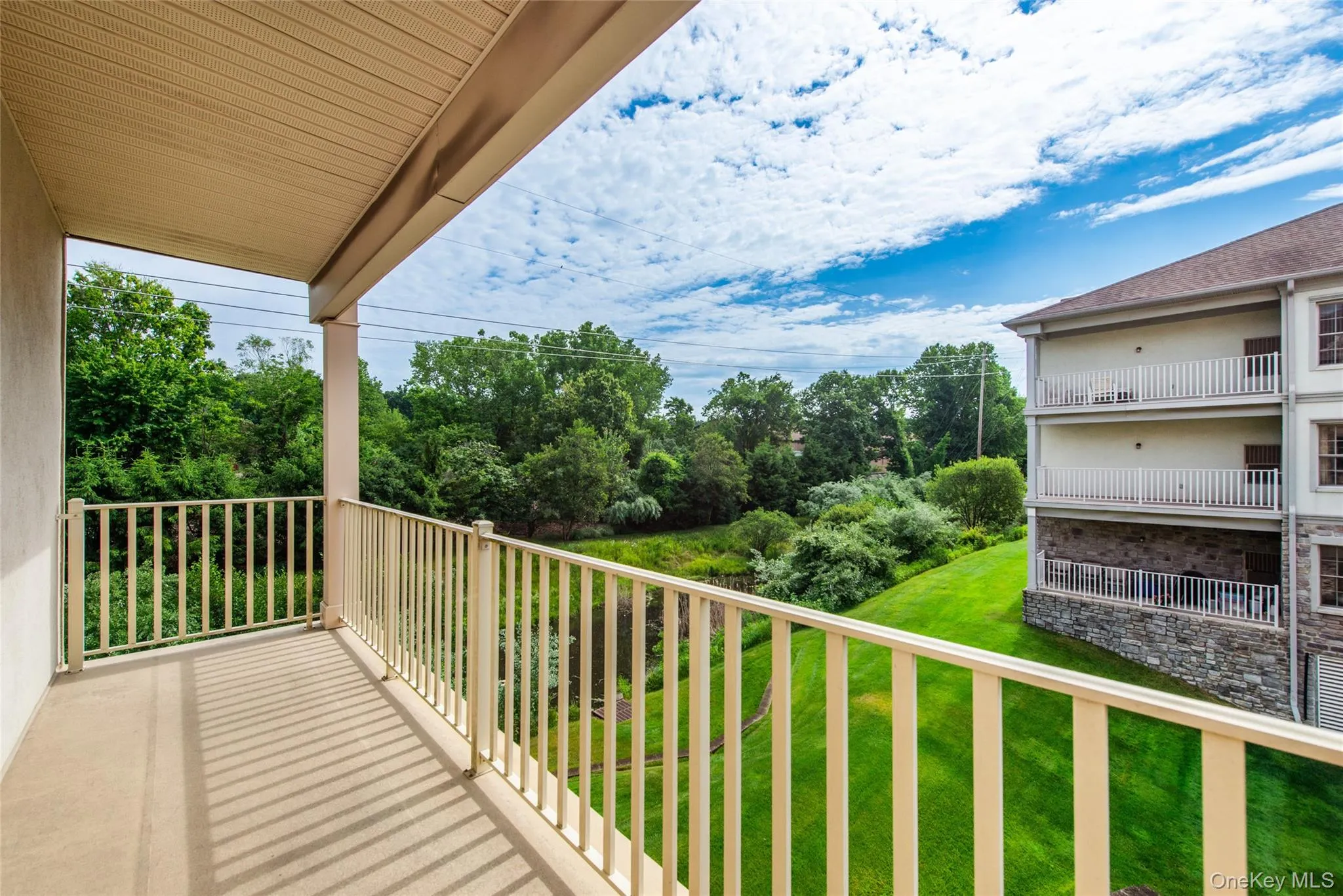 Private balcony featuring a neutral-toned concrete surface, cream-colored metal railings, and an overhead soffit Private balcony featuring a neutral-toned concrete surface, cream-colored metal railings, and an overhead soffit