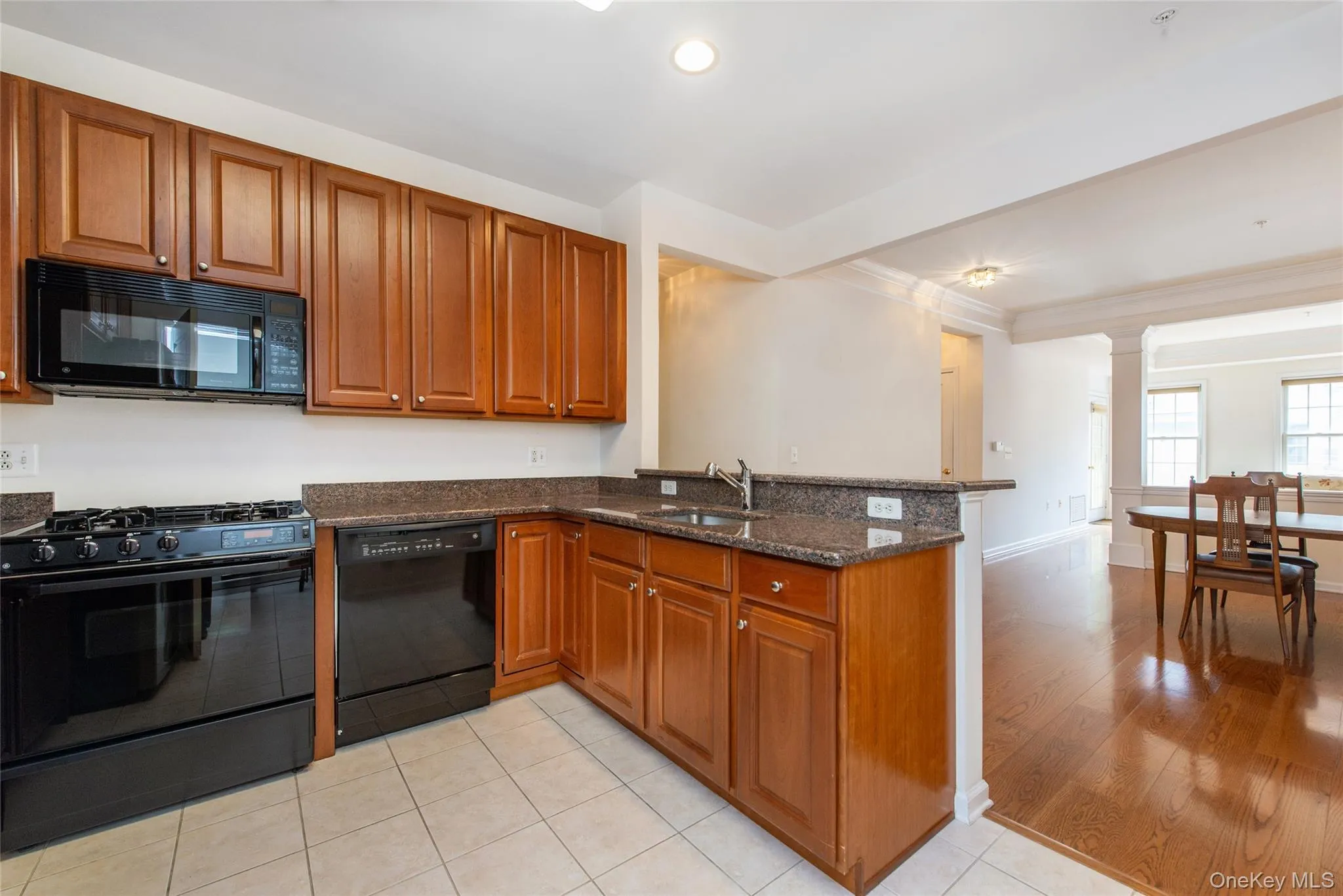 Kitchen featuring wood-finish cabinetry, black appliances including a gas range and built-in microwave, stone countertops, and tile flooring Kitchen featuring wood-finish cabinetry, black appliances including a gas range and built-in microwave, stone countertops, and tile flooring