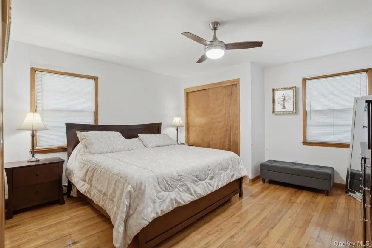 Bedroom featuring wood-finish flooring, a ceiling fan with integrated lighting, wood-trimmed windows with blinds, and two built-in closet with wood doors Bedroom featuring wood-finish flooring, a ceiling fan with integrated lighting, wood-trimmed windows with blinds, and two built-in closet with wood doors