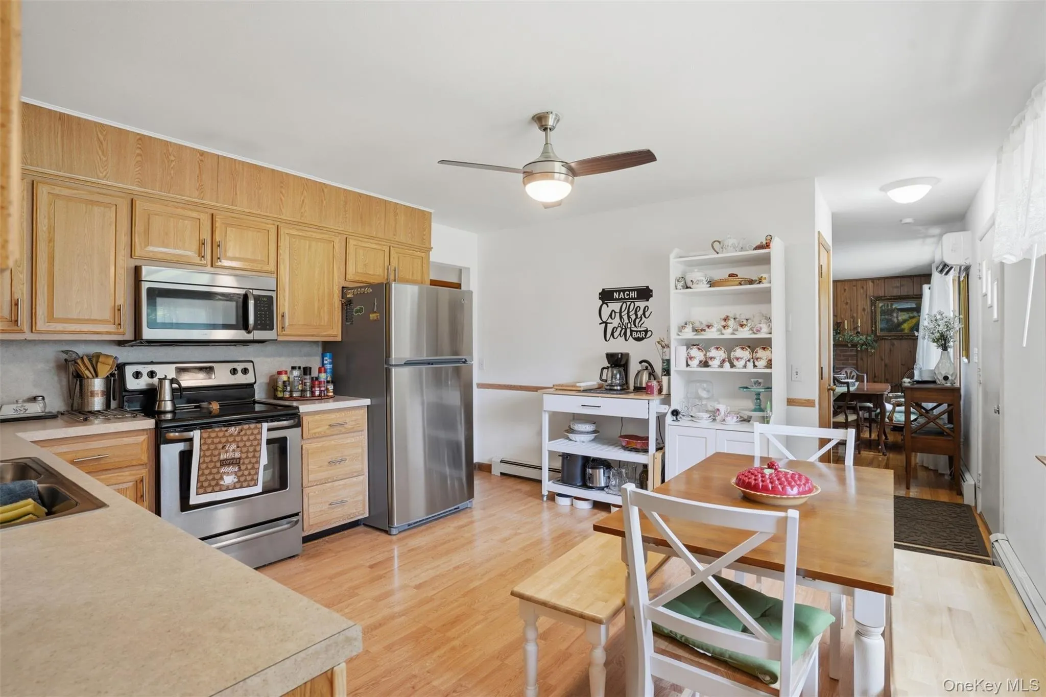 Kitchen featuring wood-finish flooring, light wood cabinetry, stainless steel appliances, and a ceiling fan with integrated lighting Kitchen featuring wood-finish flooring, light wood cabinetry, stainless steel appliances, and a ceiling fan with integrated lighting