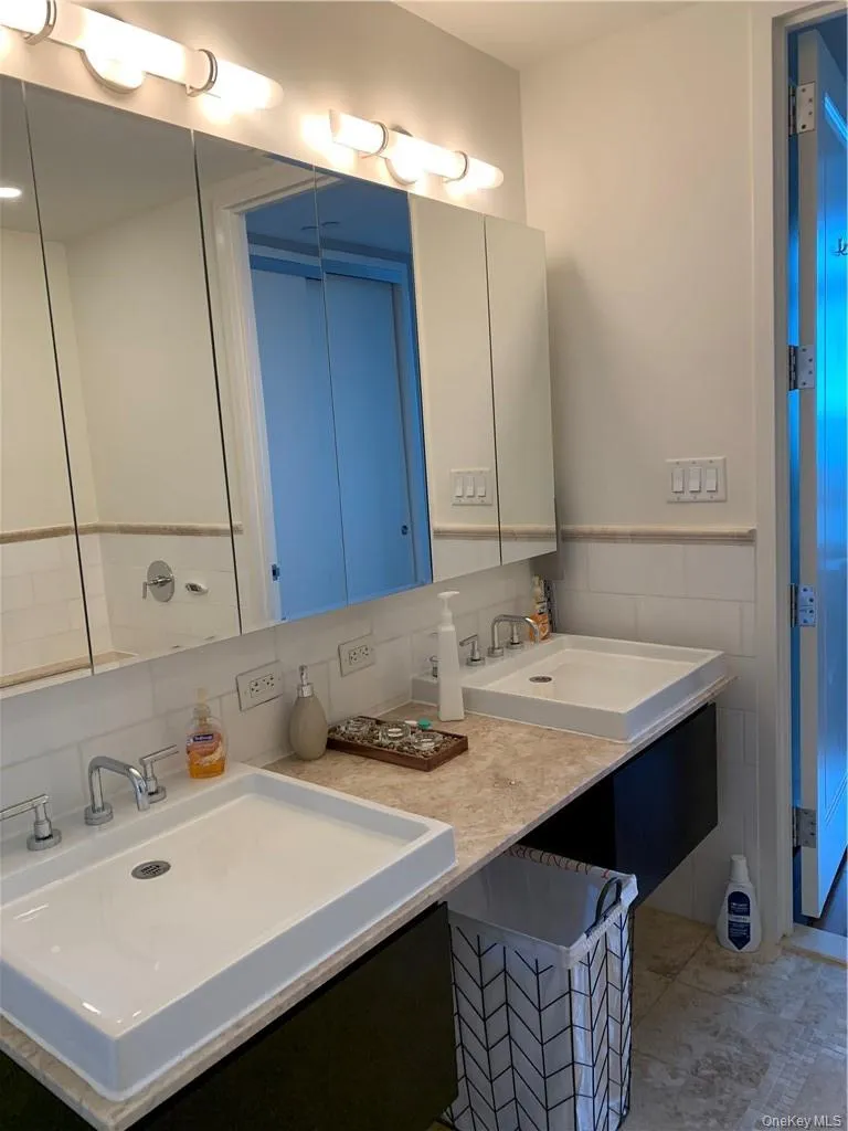 Bathroom featuring backsplash, dual vanity, tile patterned floors, and tile walls Bathroom featuring backsplash, dual vanity, tile patterned floors, and tile walls