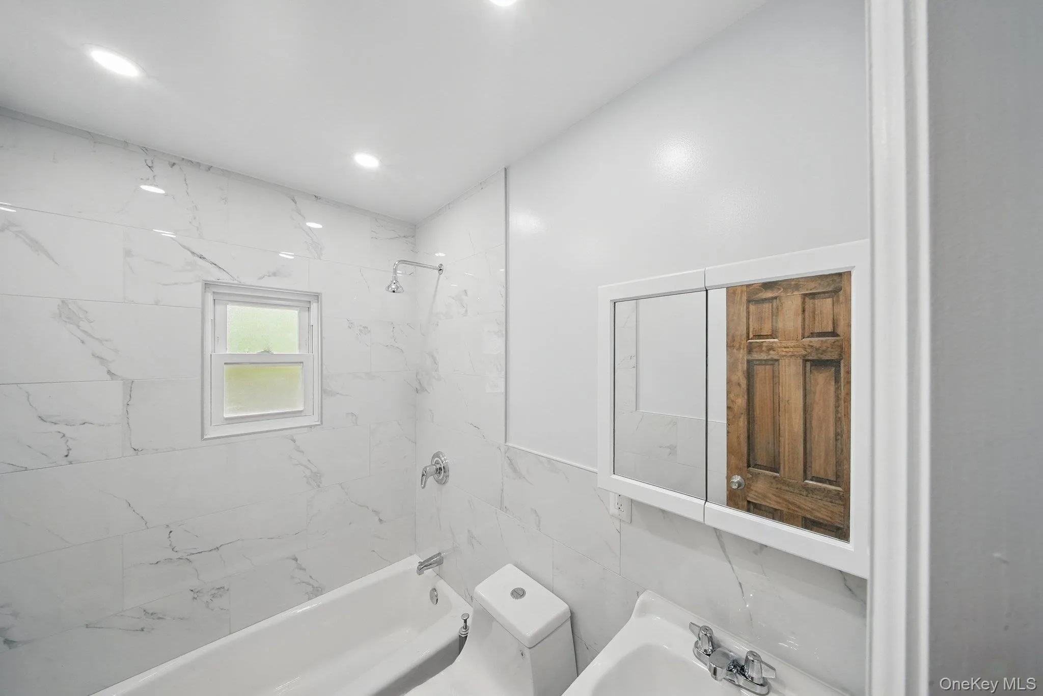 Bathroom with washtub / shower combination, toilet, a sink, and tile walls Bathroom with washtub / shower combination, toilet, a sink, and tile walls