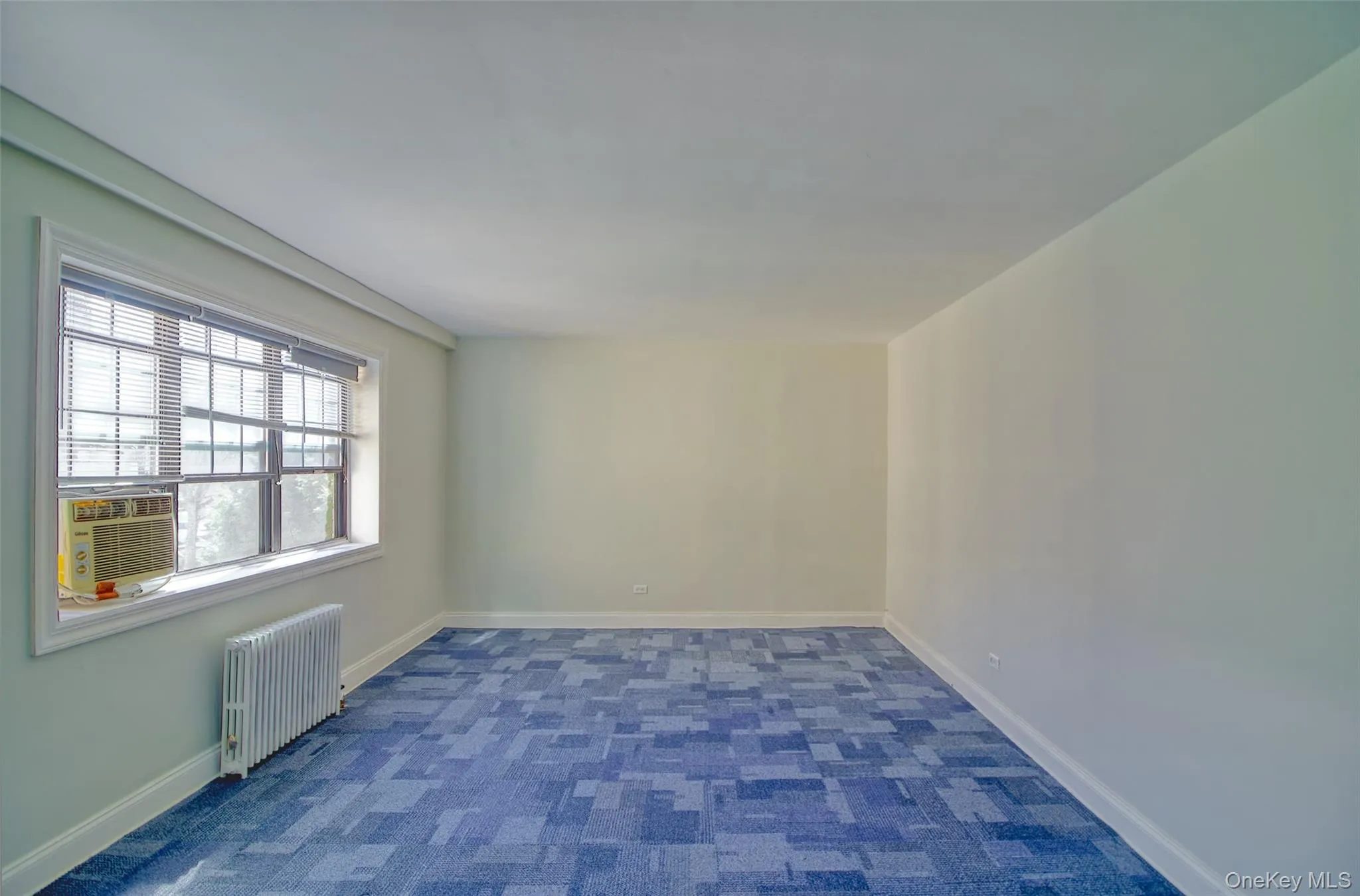 Carpeted spare room with baseboards, cooling unit, and radiator heating unit Carpeted spare room with baseboards, cooling unit, and radiator heating unit