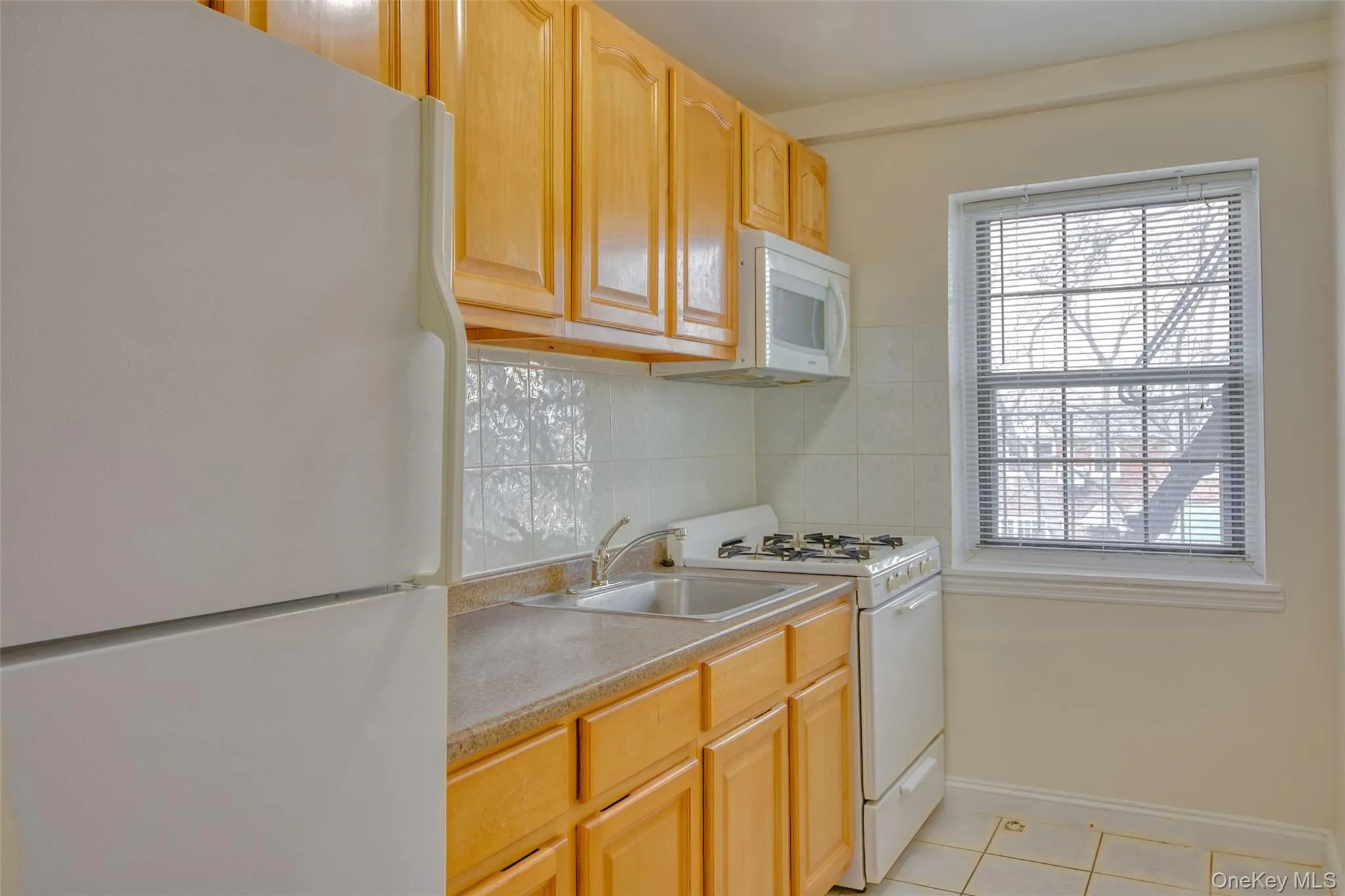 Kitchen with a healthy amount of sunlight, tasteful backsplash, light tile patterned floors, and white appliances Kitchen with a healthy amount of sunlight, tasteful backsplash, light tile patterned floors, and white appliances