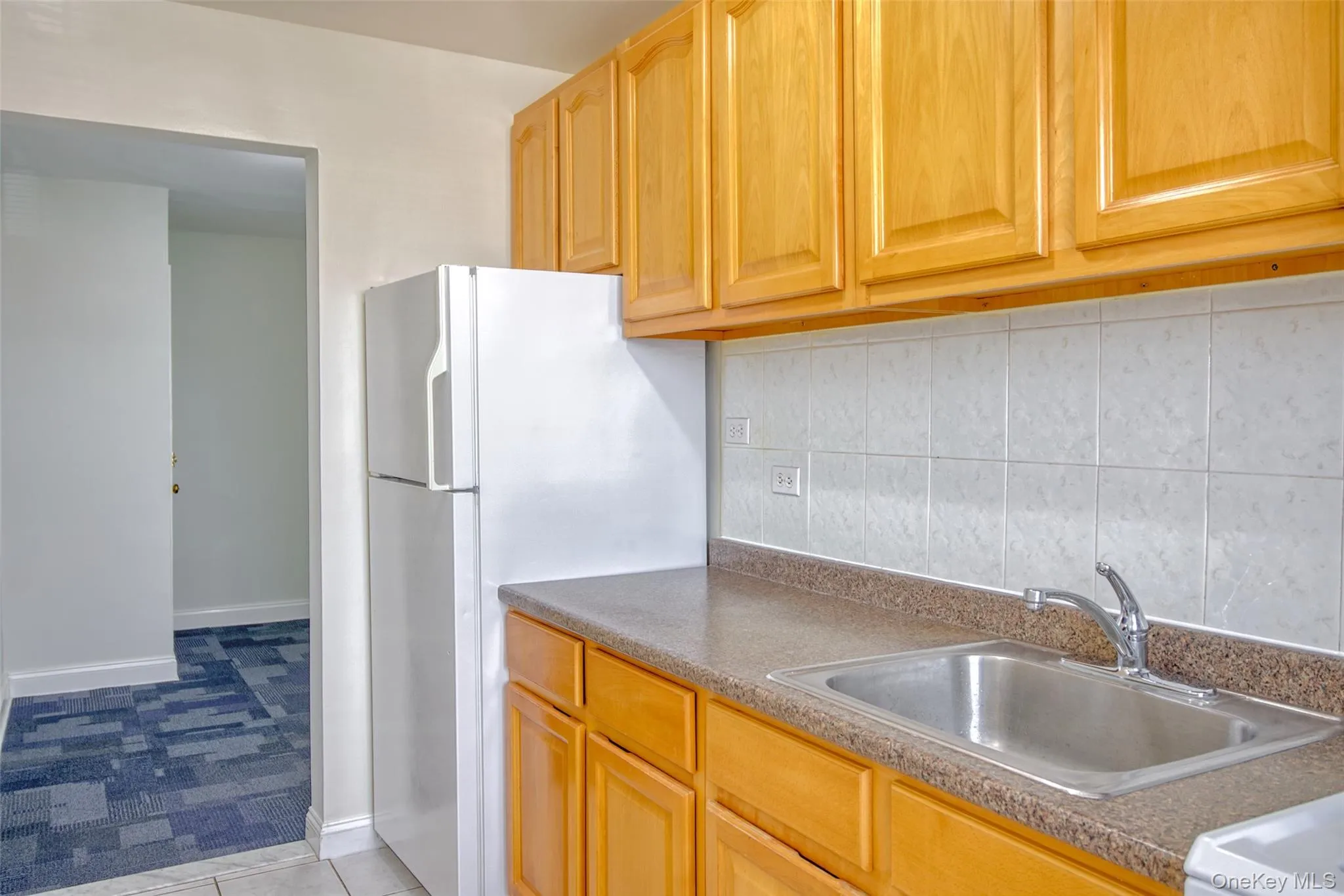 Kitchen featuring a sink, freestanding refrigerator, tasteful backsplash, baseboards, and dark countertops Kitchen featuring a sink, freestanding refrigerator, tasteful backsplash, baseboards, and dark countertops