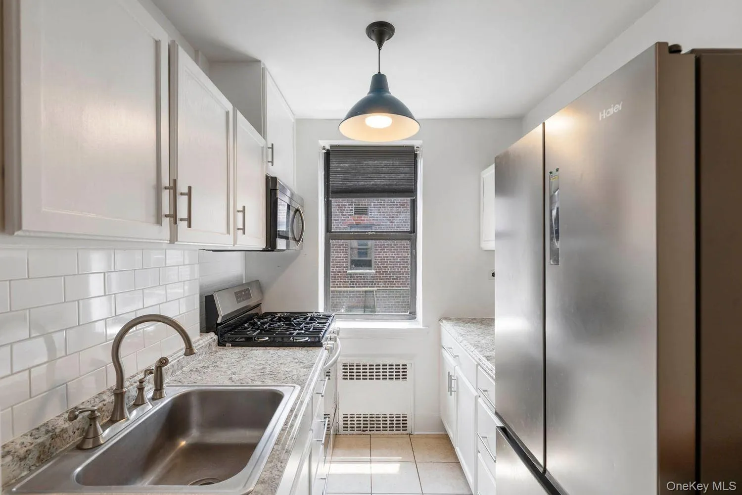Kitchen featuring appliances with stainless steel finishes, radiator heating unit, decorative backsplash, light tile patterned flooring, and white cabinetry Kitchen featuring appliances with stainless steel finishes, radiator heating unit, decorative backsplash, light tile patterned flooring, and white cabinetry