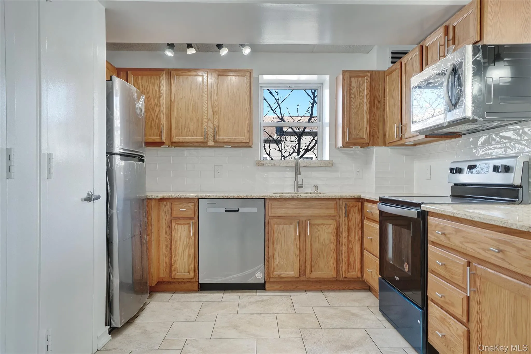 Kitchen featuring stainless steel appliances, decorative backsplash, and light stone countertops Kitchen featuring stainless steel appliances, decorative backsplash, and light stone countertops