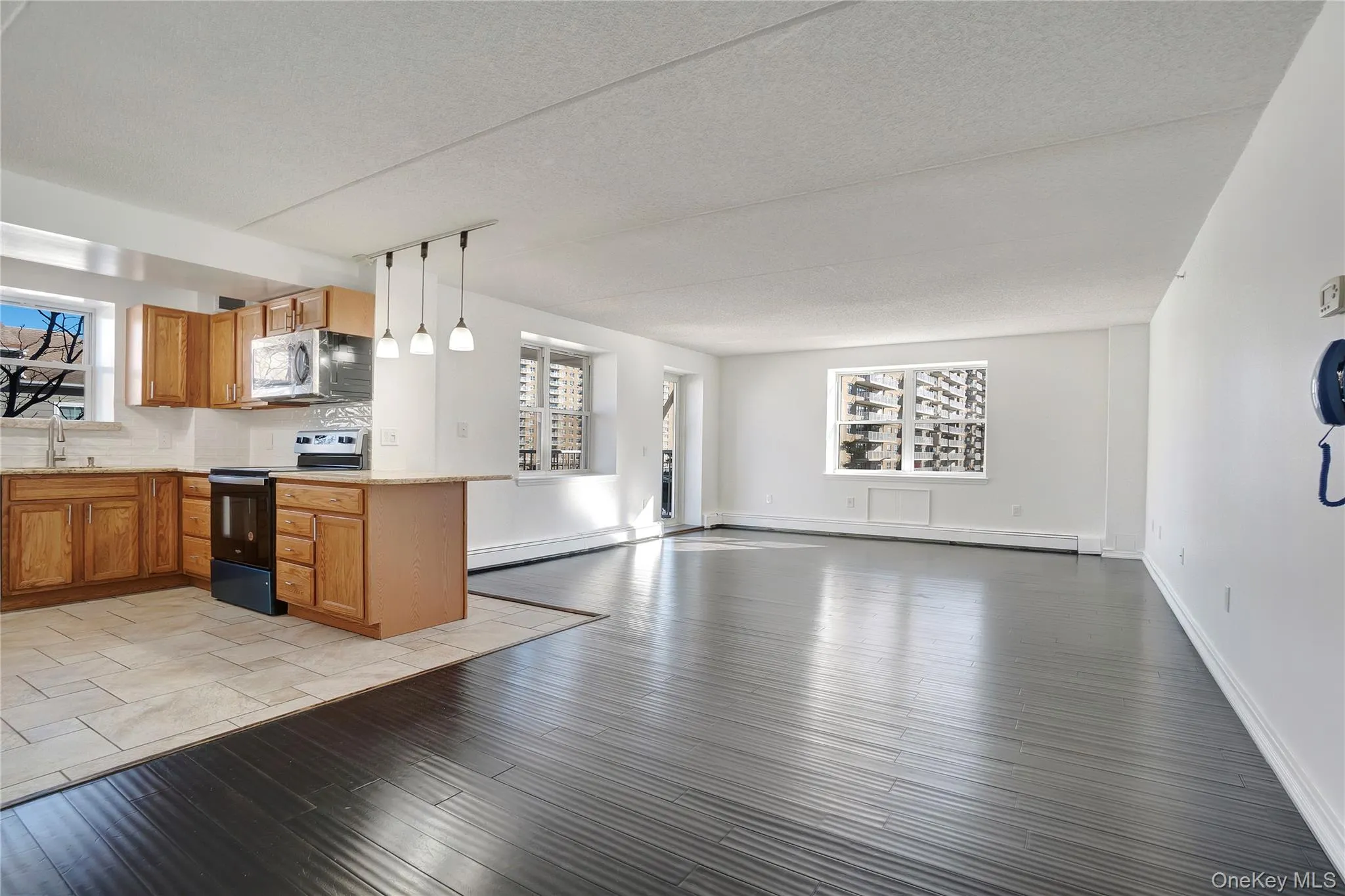 Kitchen featuring open floor plan, appliances with stainless steel finishes, light wood finished floors, brown cabinetry, and a textured ceiling Kitchen featuring open floor plan, appliances with stainless steel finishes, light wood finished floors, brown cabinetry, and a textured ceiling