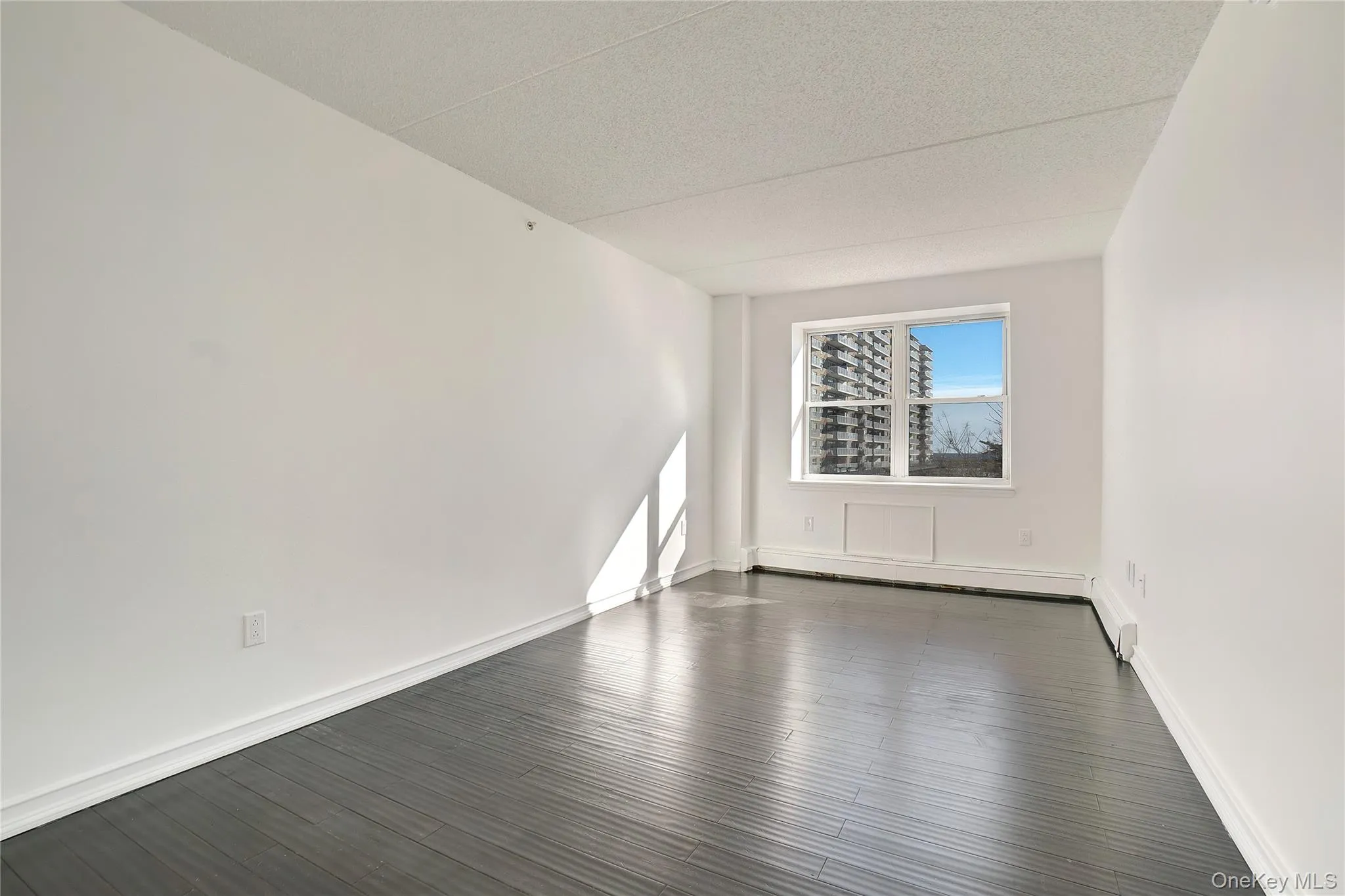 Spare room featuring dark wood finished floors, a textured ceiling, and baseboard heating Spare room featuring dark wood finished floors, a textured ceiling, and baseboard heating