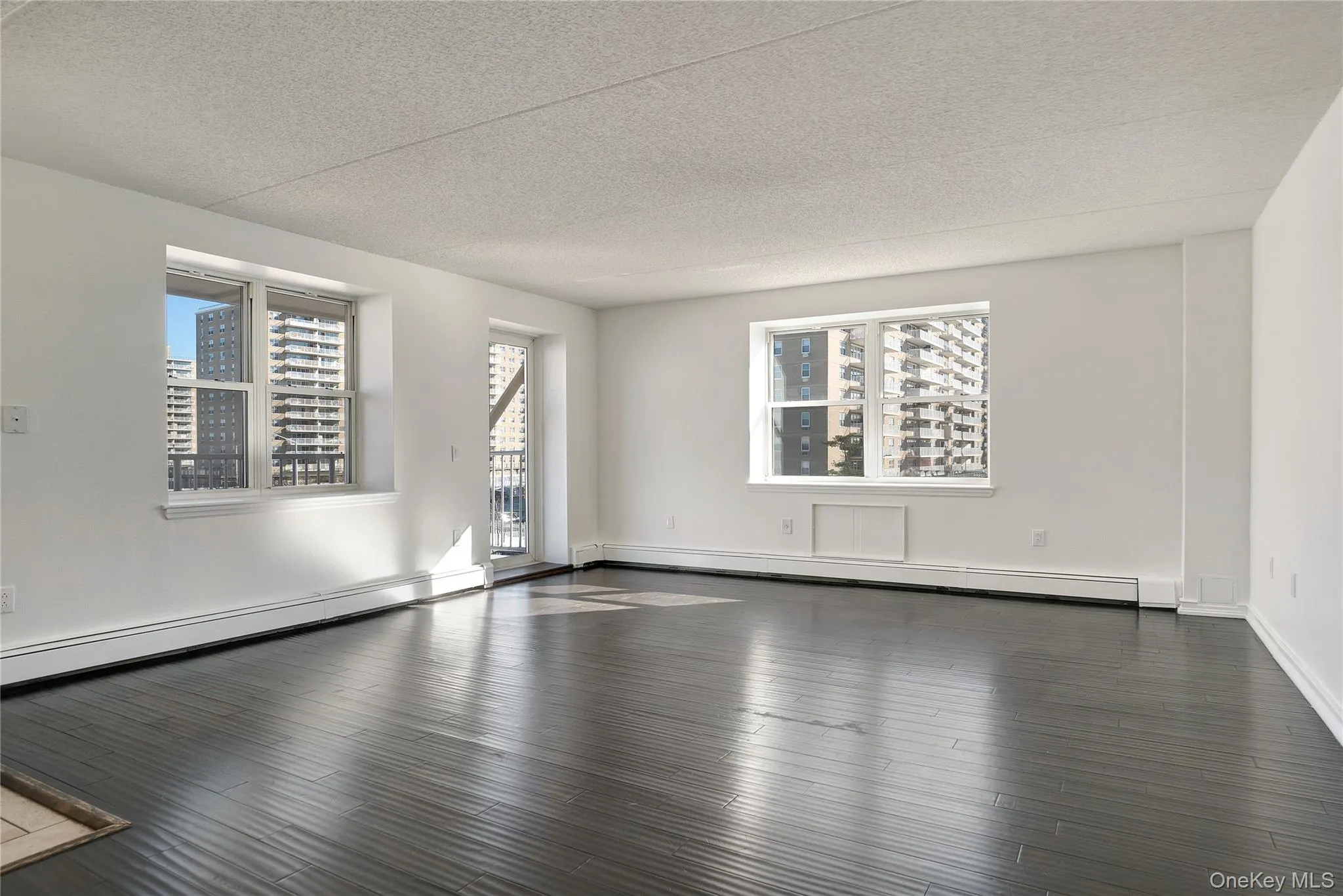 Empty room with a textured ceiling, baseboard heating, dark wood-type flooring, and a view of city Empty room with a textured ceiling, baseboard heating, dark wood-type flooring, and a view of city
