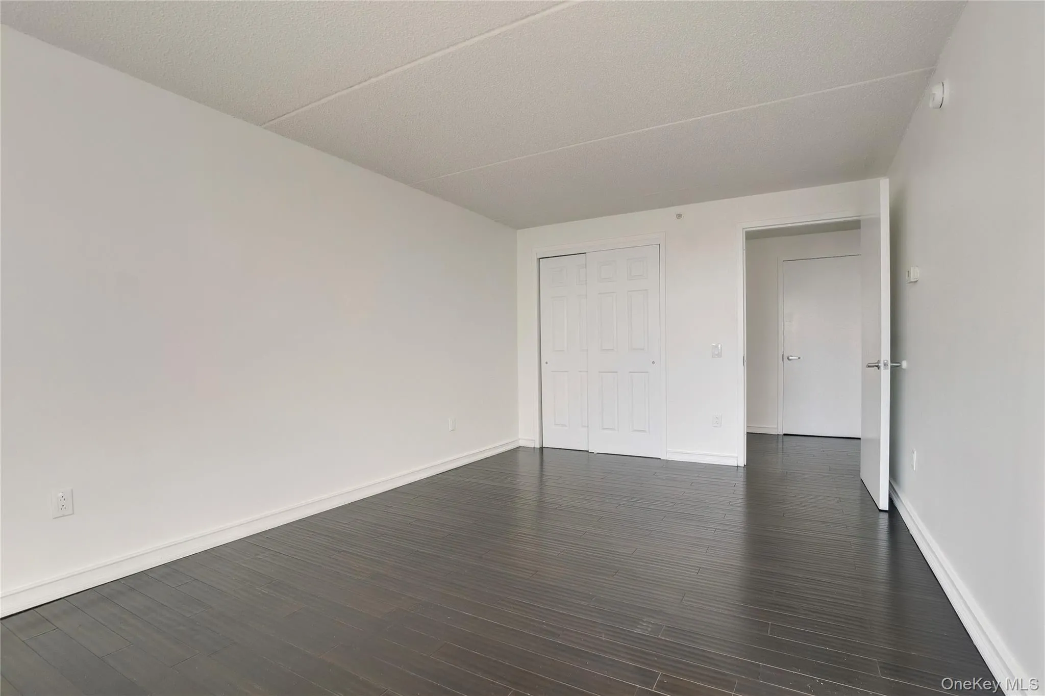 Unfurnished room featuring dark wood-type flooring and a textured ceiling Unfurnished room featuring dark wood-type flooring and a textured ceiling
