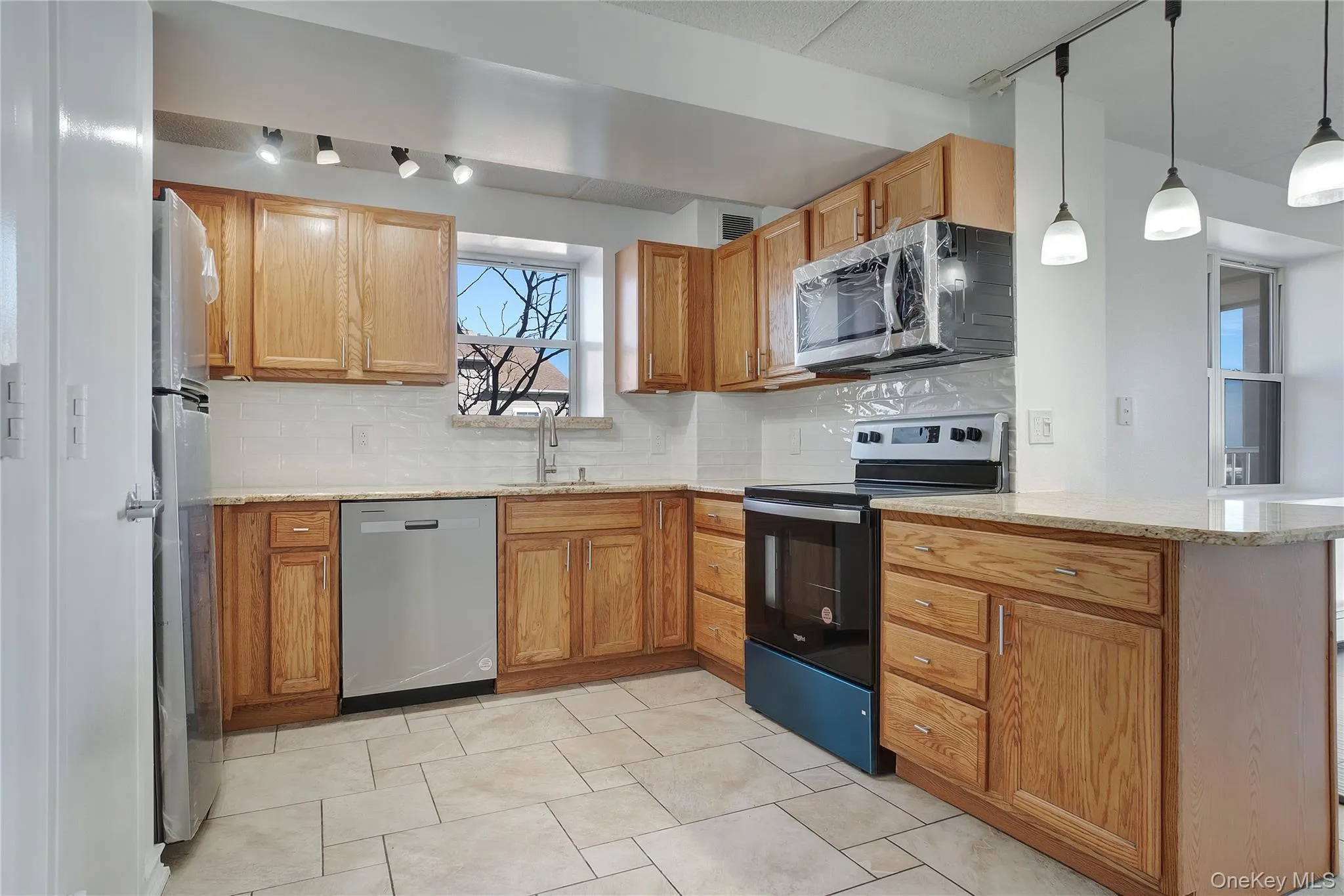 Kitchen with stainless steel appliances, tasteful backsplash, light stone countertops, decorative light fixtures, and a peninsula Kitchen with stainless steel appliances, tasteful backsplash, light stone countertops, decorative light fixtures, and a peninsula