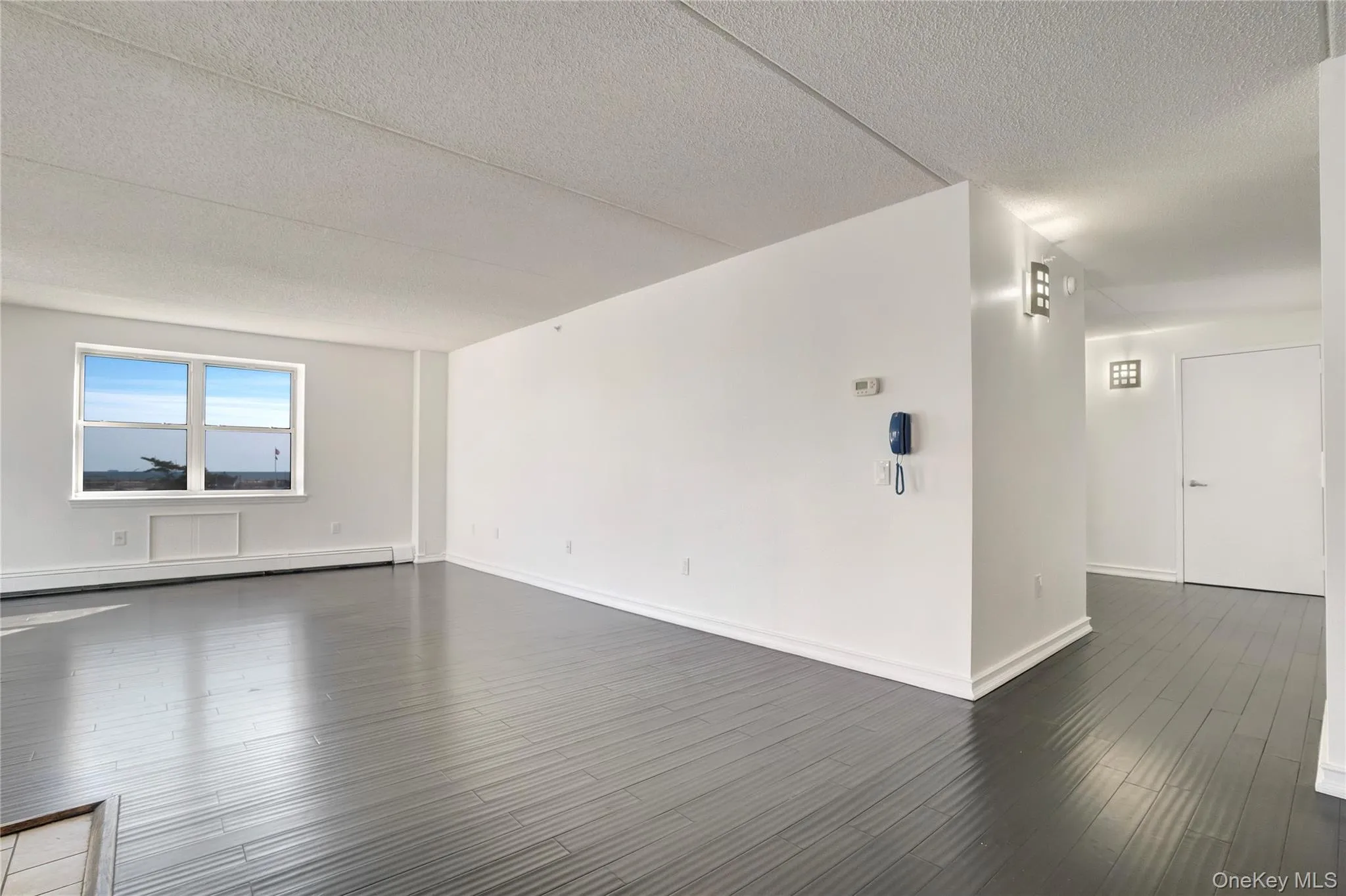 Unfurnished room featuring a textured ceiling, dark wood-type flooring, and a baseboard radiator Unfurnished room featuring a textured ceiling, dark wood-type flooring, and a baseboard radiator