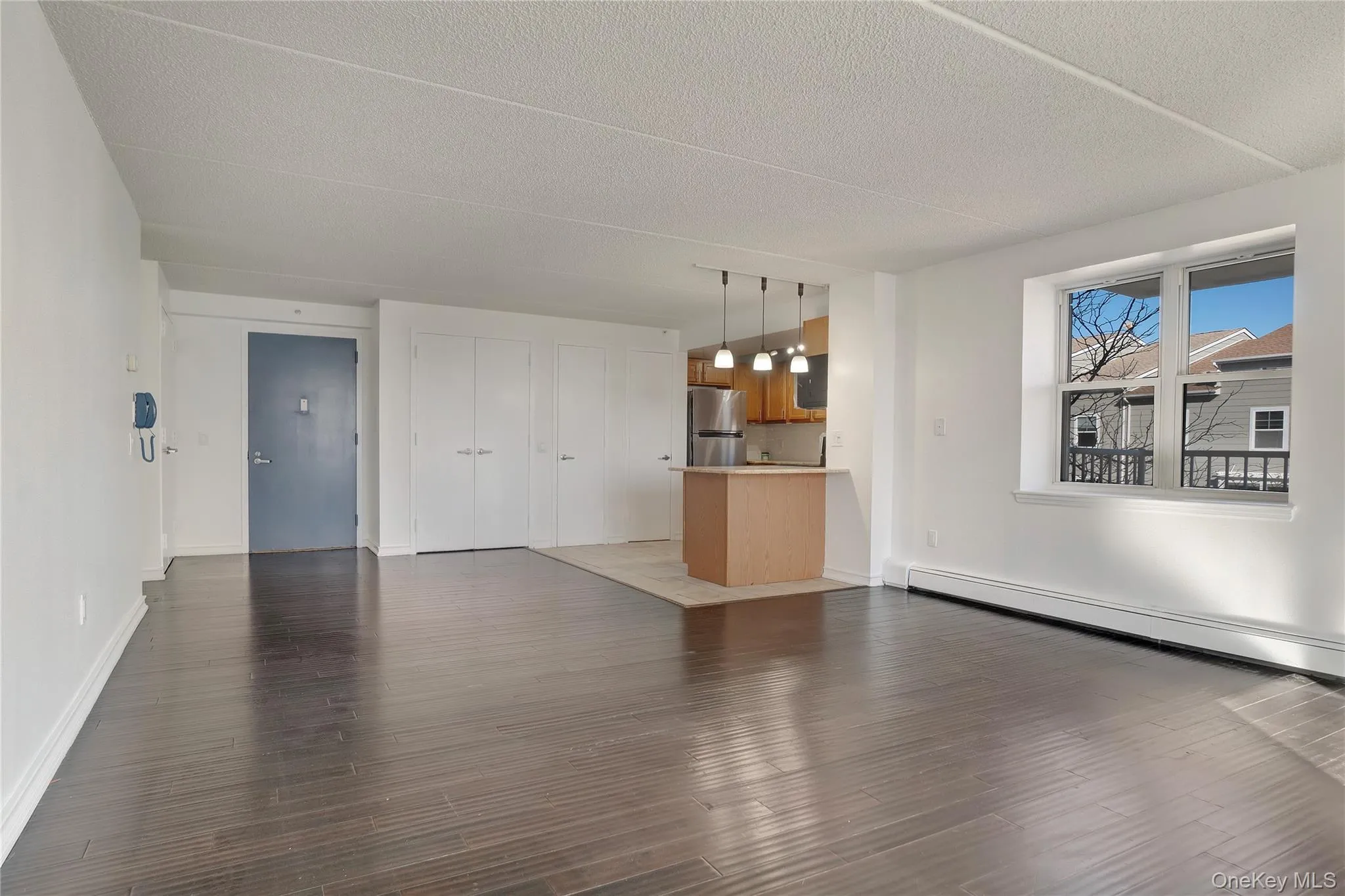 Unfurnished living room featuring wood finished floors, a baseboard radiator, and a textured ceiling Unfurnished living room featuring wood finished floors, a baseboard radiator, and a textured ceiling