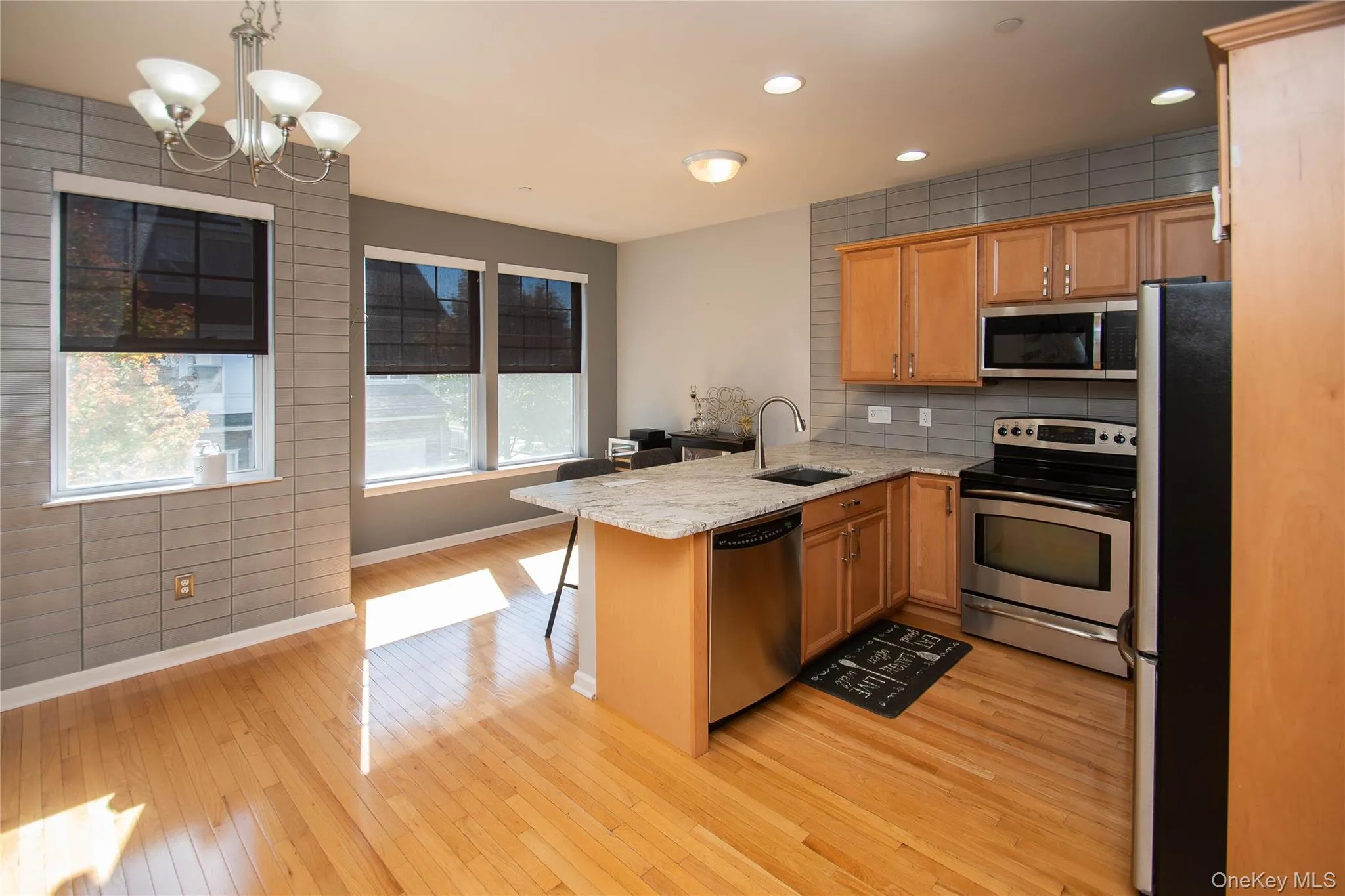Kitchen with appliances with stainless steel finishes, a kitchen bar, tasteful backsplash, light wood-style floors, and recessed lighting Kitchen with appliances with stainless steel finishes, a kitchen bar, tasteful backsplash, light wood-style floors, and recessed lighting