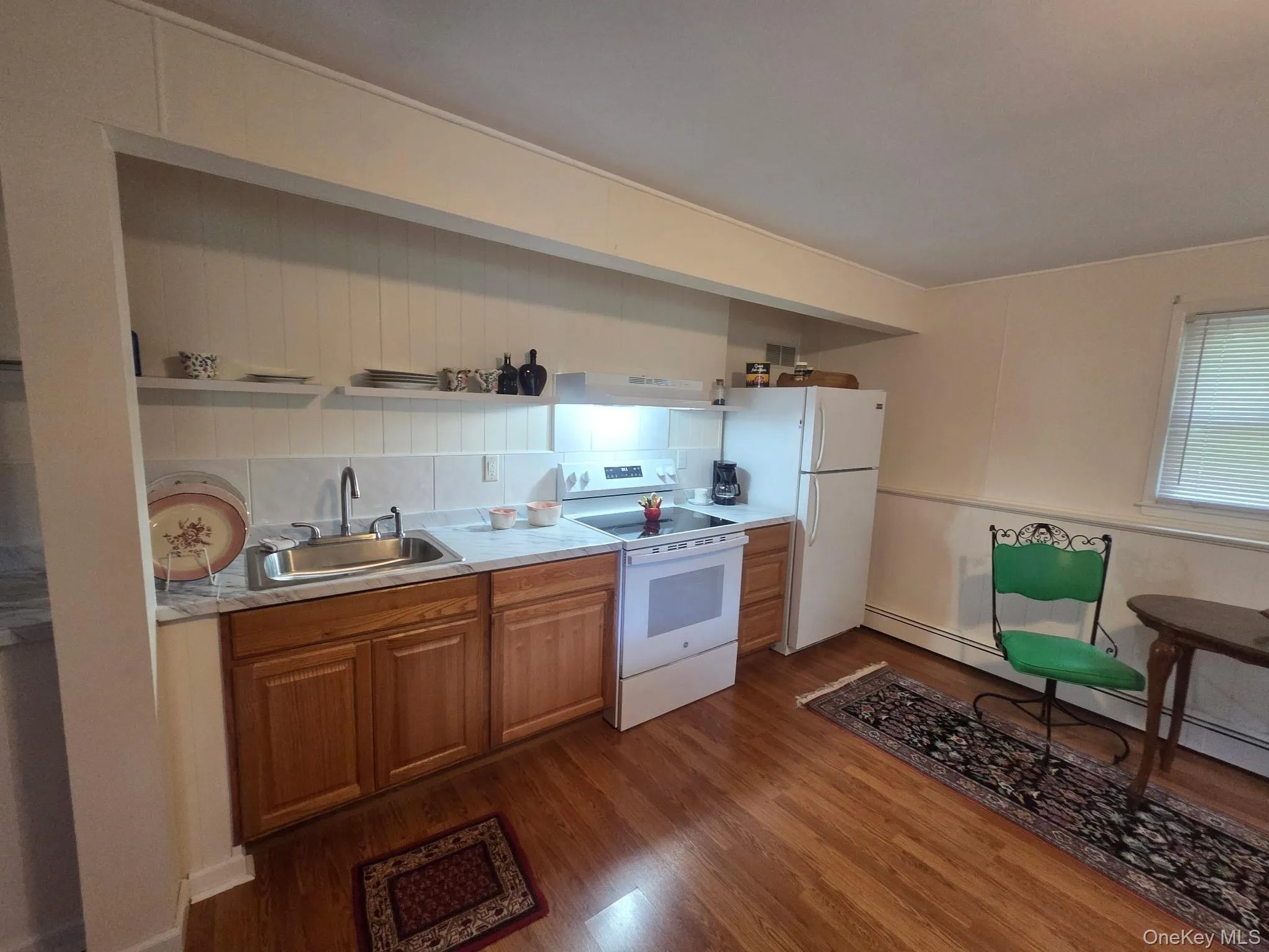 Compact kitchen featuring wood-finish flooring, white paneled walls, and a white tile backsplash Compact kitchen featuring wood-finish flooring, white paneled walls, and a white tile backsplash