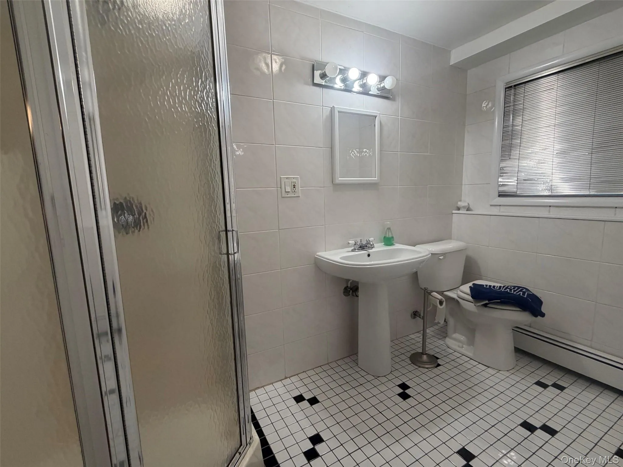 Pedestal sink with chrome faucet, white tiled walls, and black and white mosaic tile flooring Pedestal sink with chrome faucet, white tiled walls, and black and white mosaic tile flooring