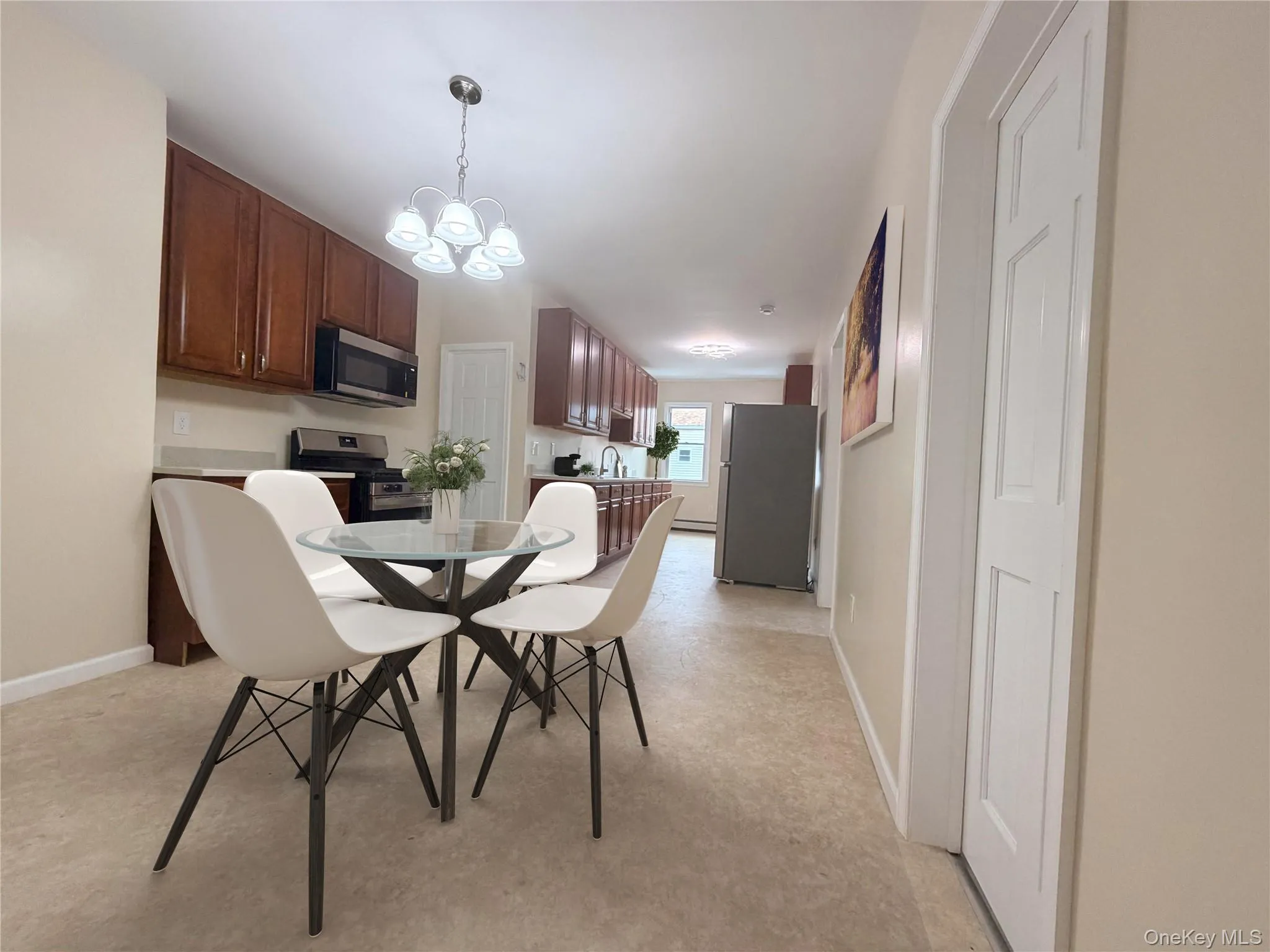 Kitchen and dining area featuring wood cabinetry, stainless steel appliances, light-toned countertops, and a ceiling-mounted light fixture Kitchen and dining area featuring wood cabinetry, stainless steel appliances, light-toned countertops, and a ceiling-mounted light fixture