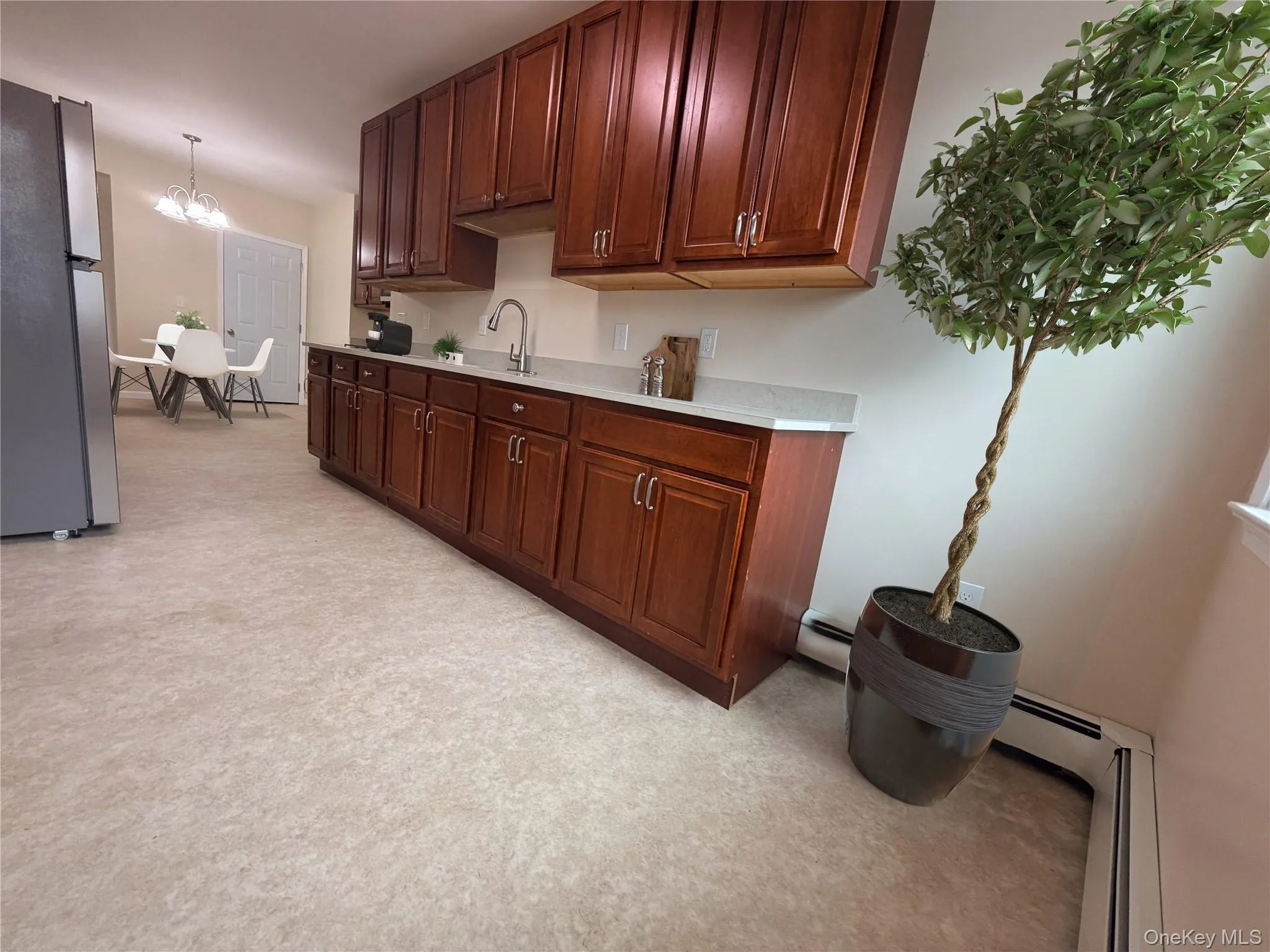 Spacious kitchen featuring extensive dark wood cabinetry, light-toned countertops, and a stainless steel sink with a gooseneck faucet Spacious kitchen featuring extensive dark wood cabinetry, light-toned countertops, and a stainless steel sink with a gooseneck faucet