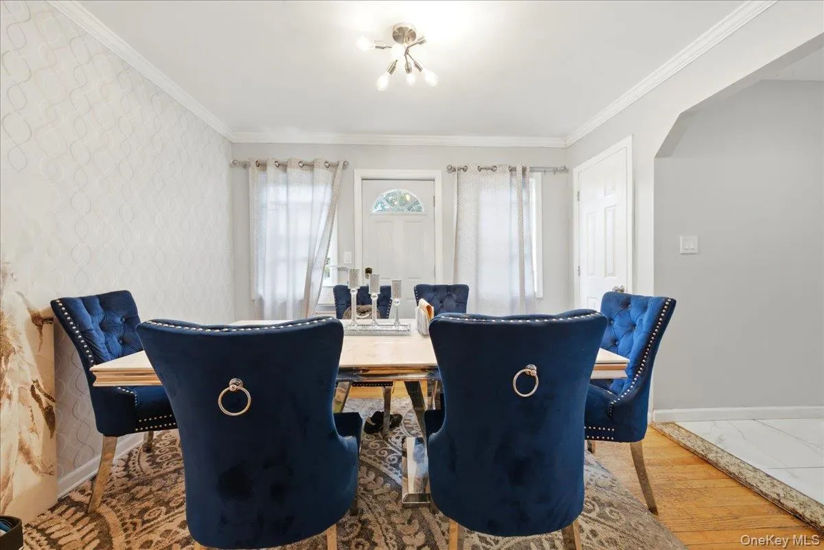 Dining area featuring wood-finish flooring, a decorative accent wall, crown molding, and a white paneled door Dining area featuring wood-finish flooring, a decorative accent wall, crown molding, and a white paneled door