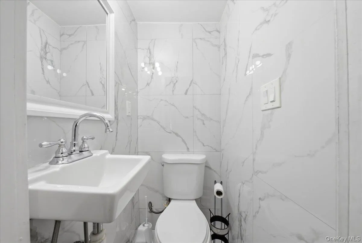 Contemporary bathroom featuring white and gray marble-look wall tiling, a white rectangular wall-mounted sink with chrome faucet, and a white toilet Contemporary bathroom featuring white and gray marble-look wall tiling, a white rectangular wall-mounted sink with chrome faucet, and a white toilet