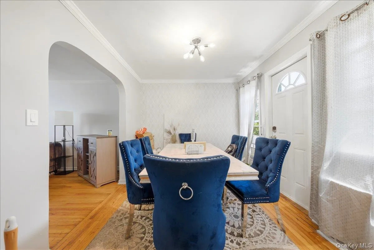 Archway opening from a dining area featuring wood-finish flooring, crown molding, and a front entry door with a transom window Archway opening from a dining area featuring wood-finish flooring, crown molding, and a front entry door with a transom window