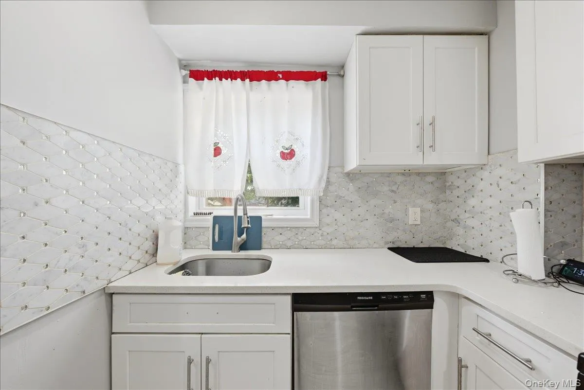 Kitchen featuring white shaker-style cabinetry, stainless steel sink with a modern faucet, light-toned countertops, and a tiled backsplash Kitchen featuring white shaker-style cabinetry, stainless steel sink with a modern faucet, light-toned countertops, and a tiled backsplash