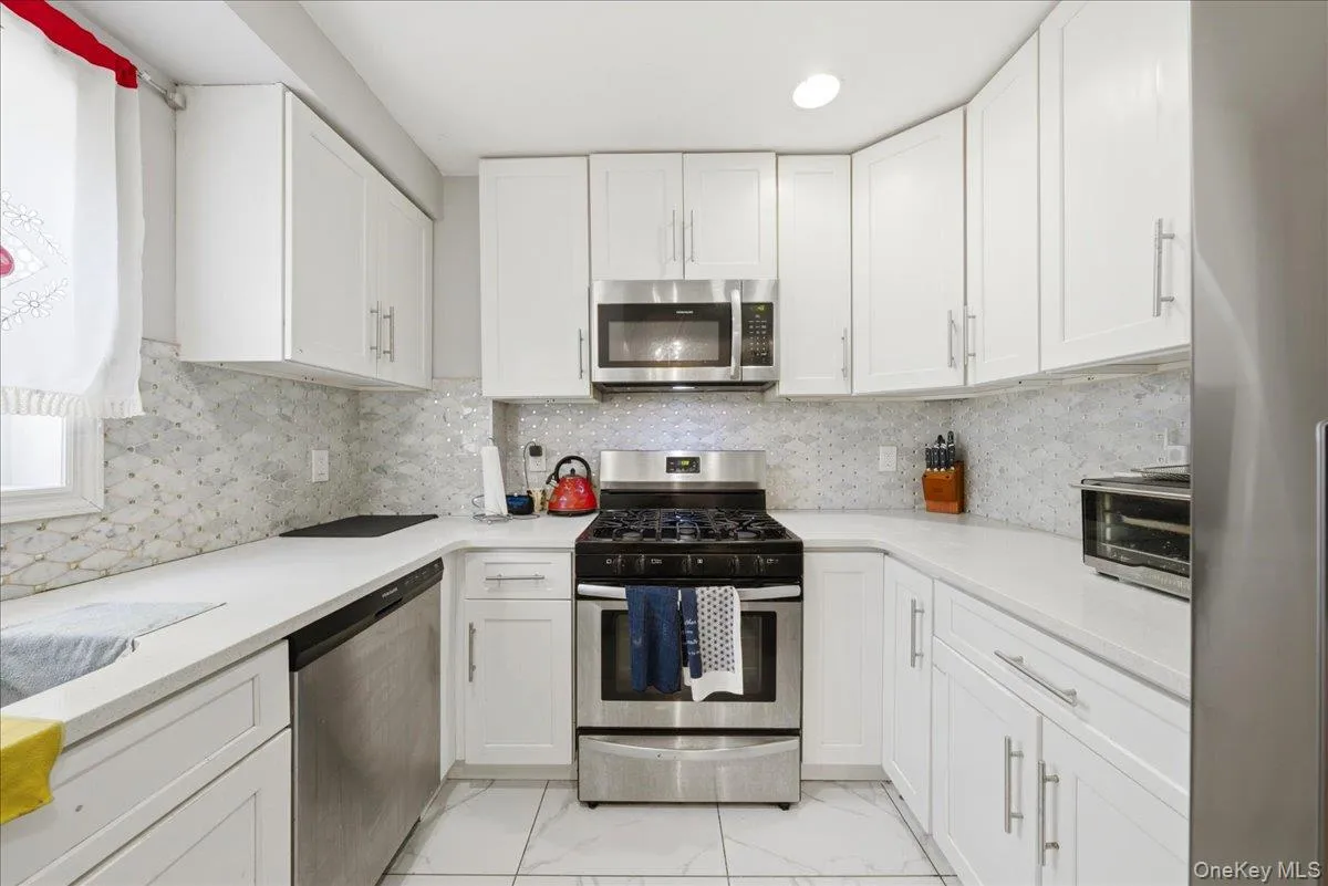 U-shaped kitchen featuring white cabinetry, light countertops, and a patterned tile backsplash U-shaped kitchen featuring white cabinetry, light countertops, and a patterned tile backsplash