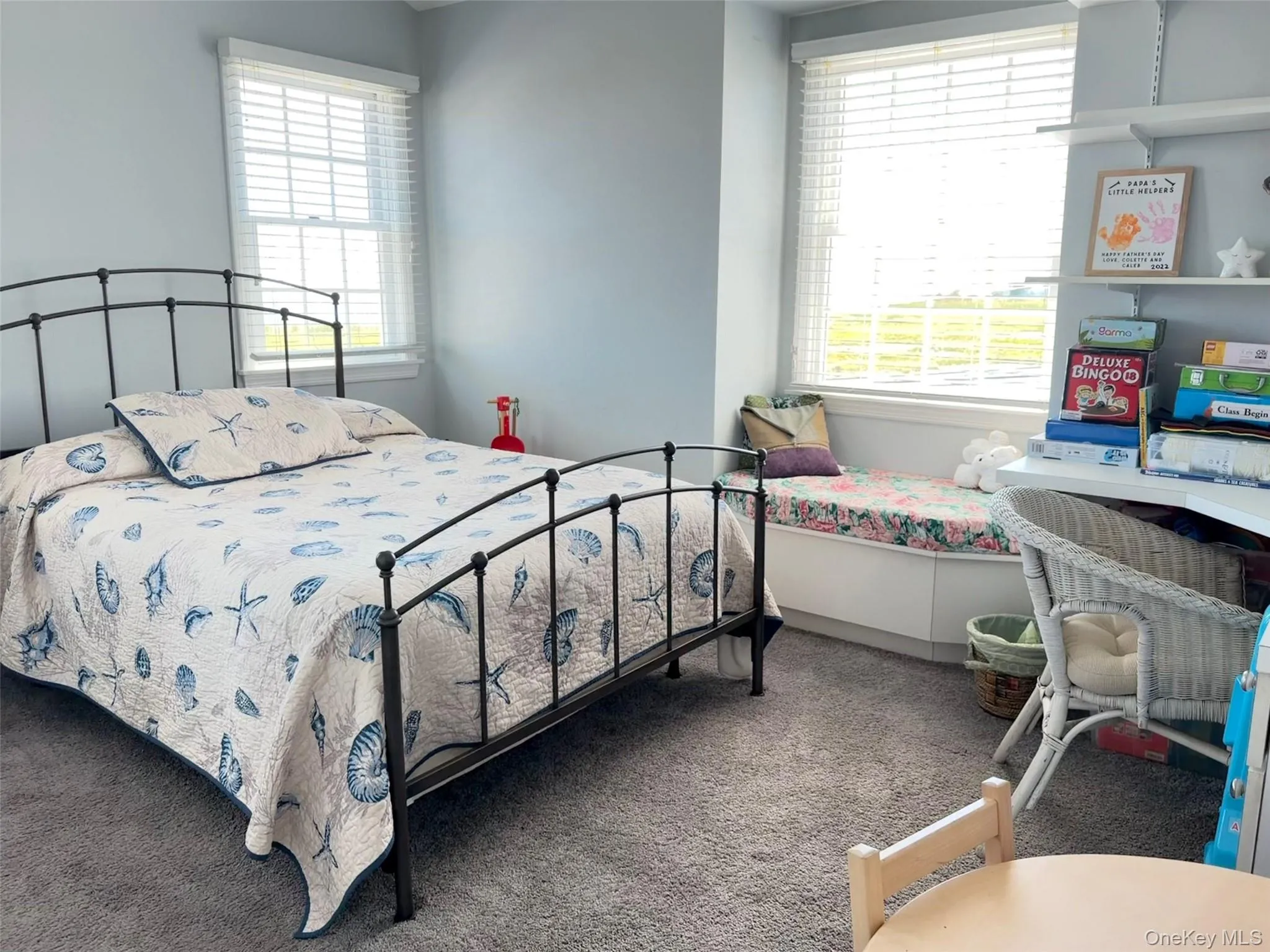 Carpeted room featuring a built-in window seat with storage, two large windows with blinds, and light-toned wall paint Carpeted room featuring a built-in window seat with storage, two large windows with blinds, and light-toned wall paint