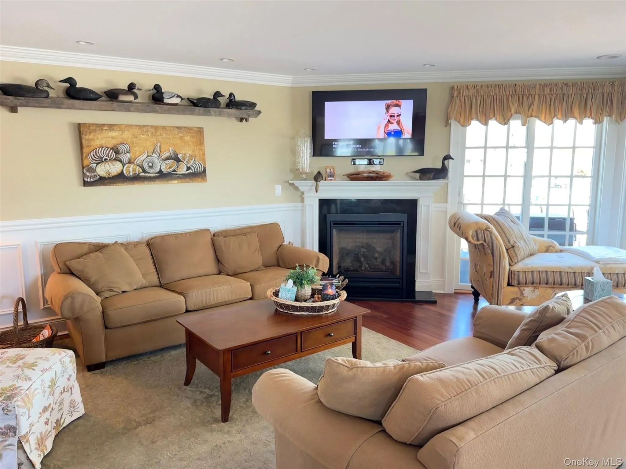 Living area featuring a fireplace with a black surround and white mantel, crown molding, chair rail molding, recessed lighting, and wood-finish flooring Living area featuring a fireplace with a black surround and white mantel, crown molding, chair rail molding, recessed lighting, and wood-finish flooring